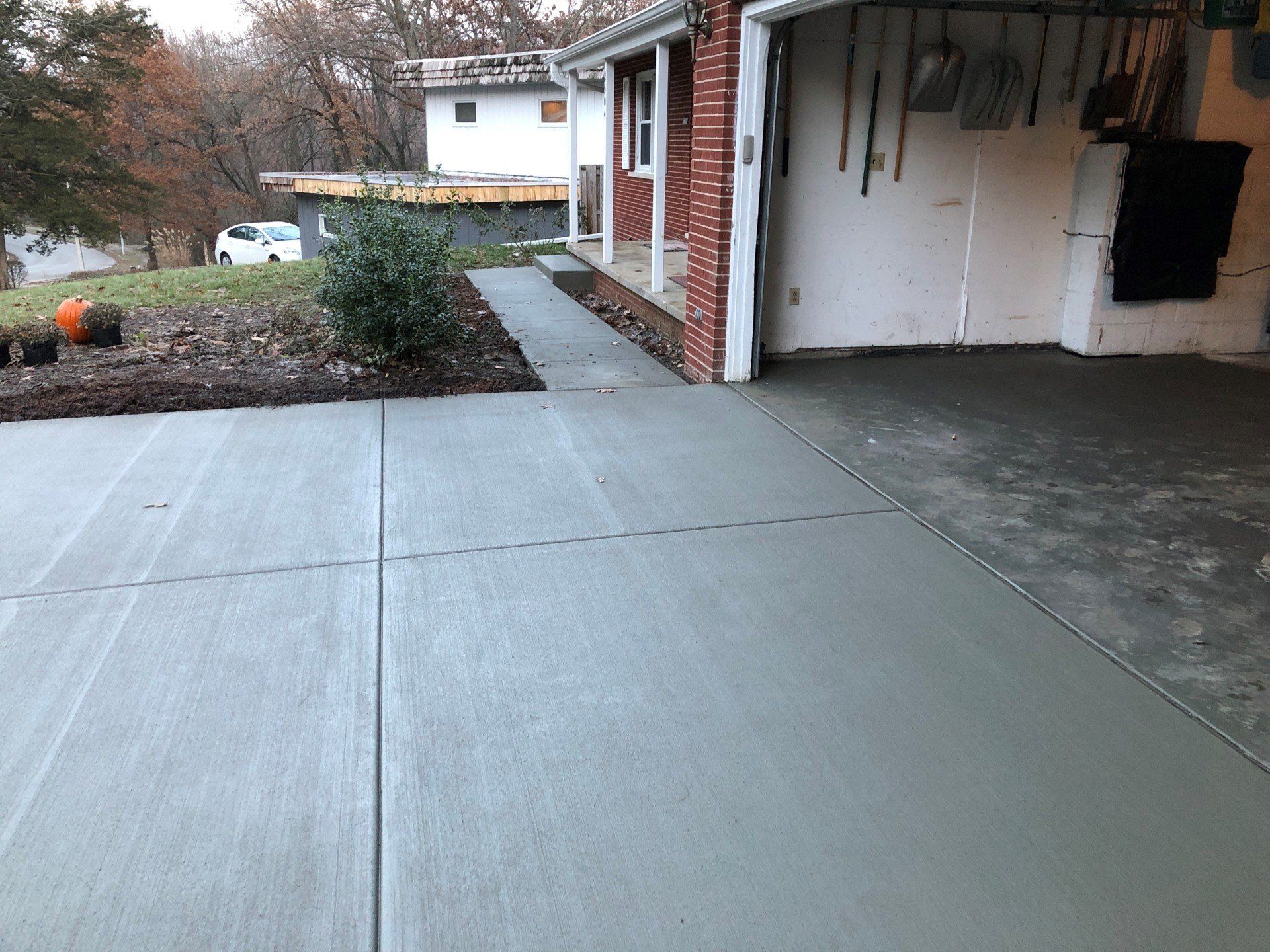 Freshly poured concrete driveway and sidewalk next to a house with an open garage.