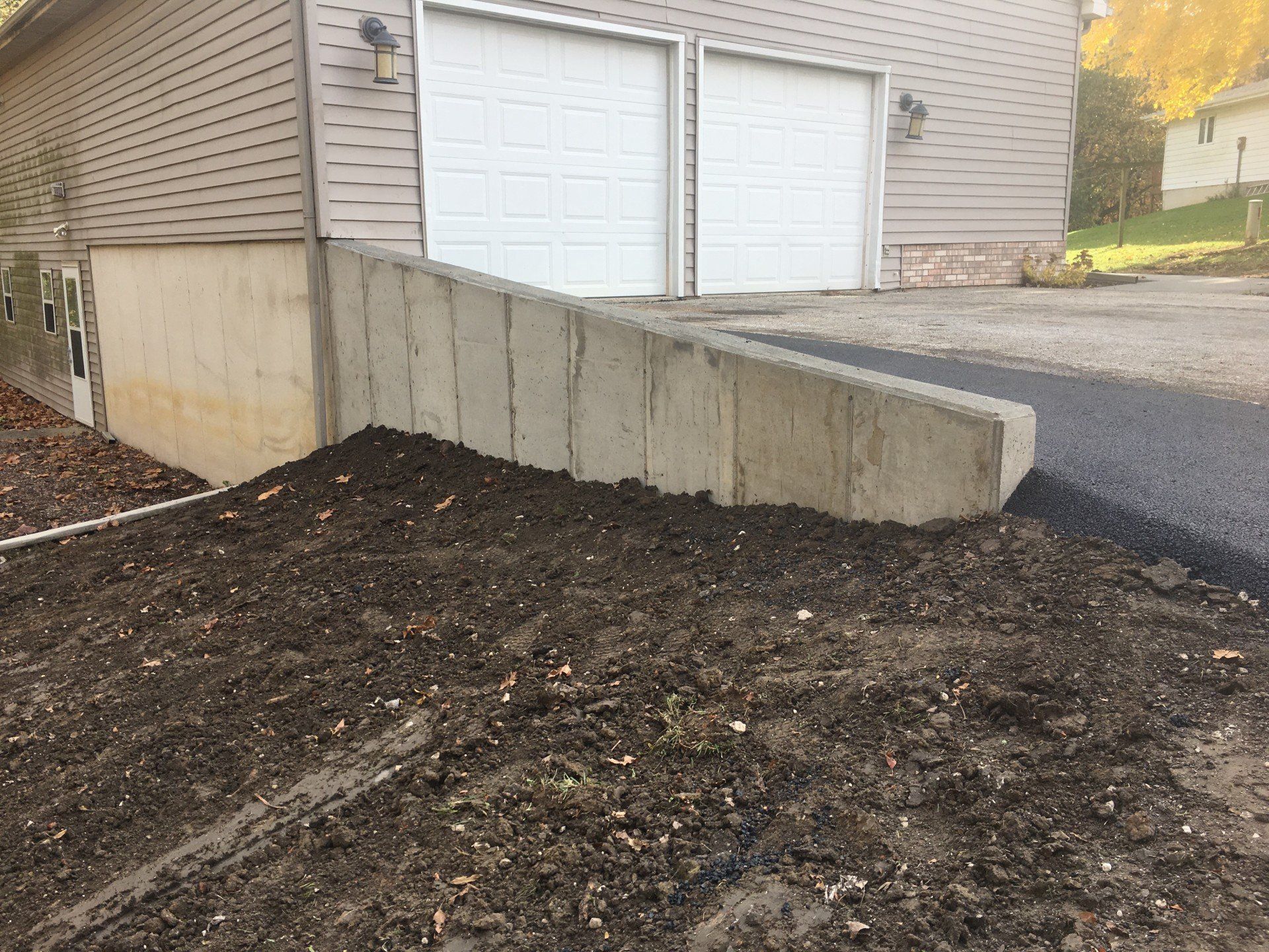 Concrete retaining wall next to garage with dirt and asphalt.