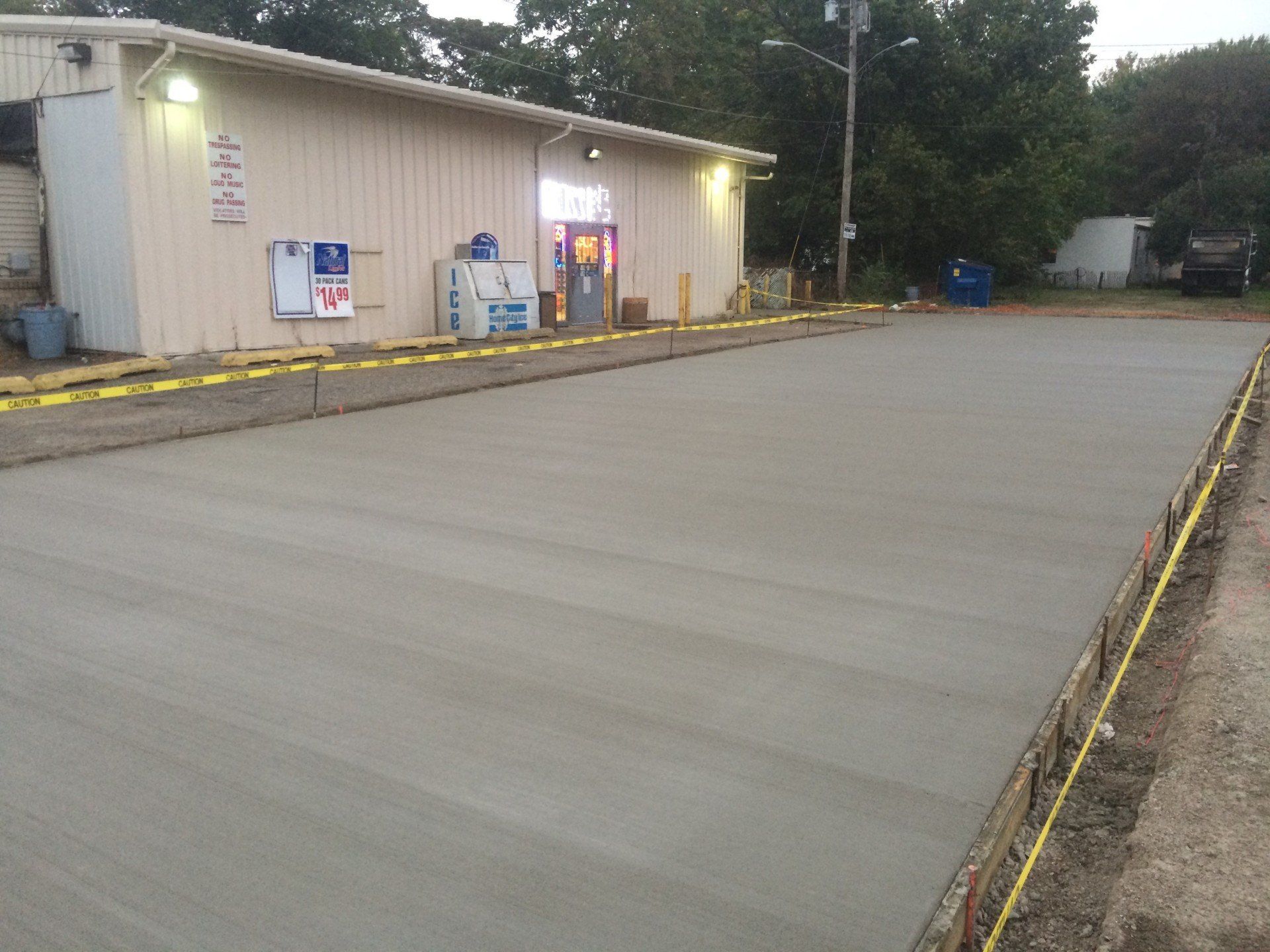 Newly poured concrete slab in front of a tan building. Yellow caution tape lines edges.