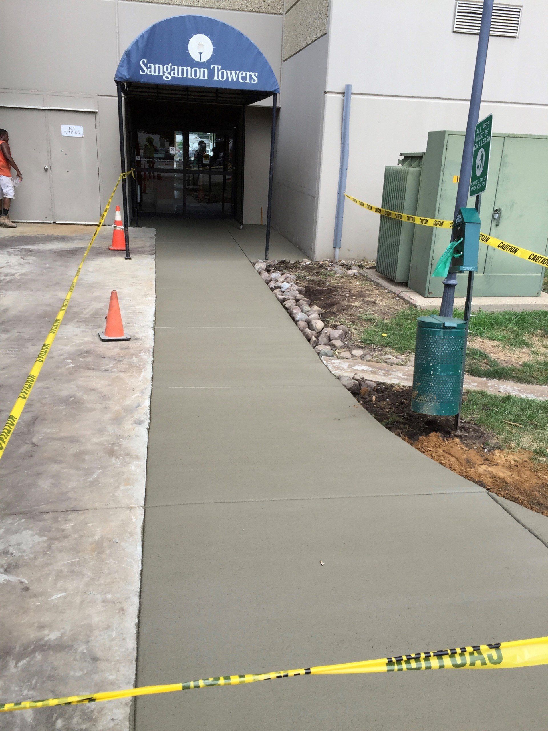 New concrete ramp leads to building entrance, with caution tape and cones.