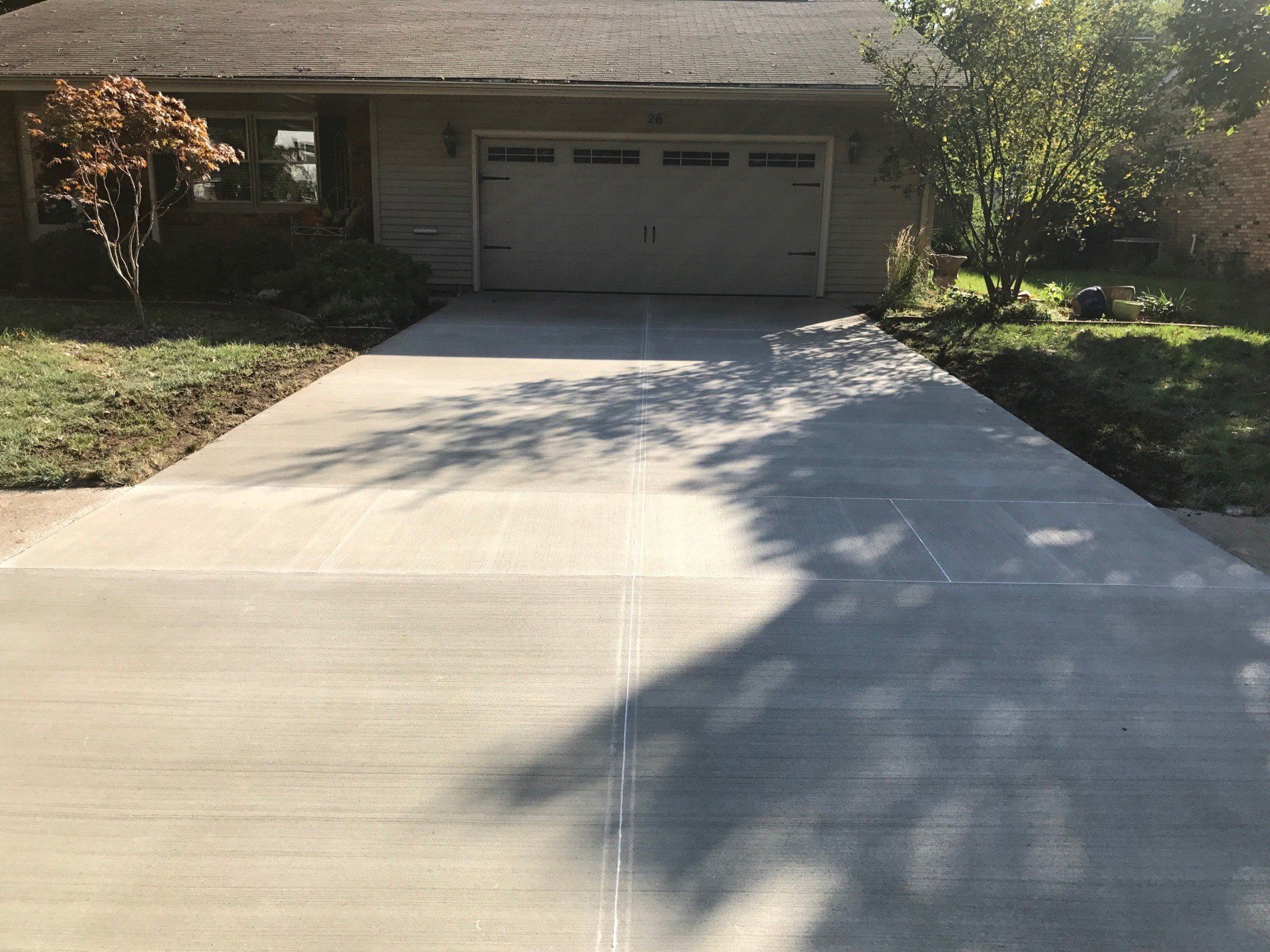 Newly poured concrete driveway in front of a house, with shadow of a tree over it.
