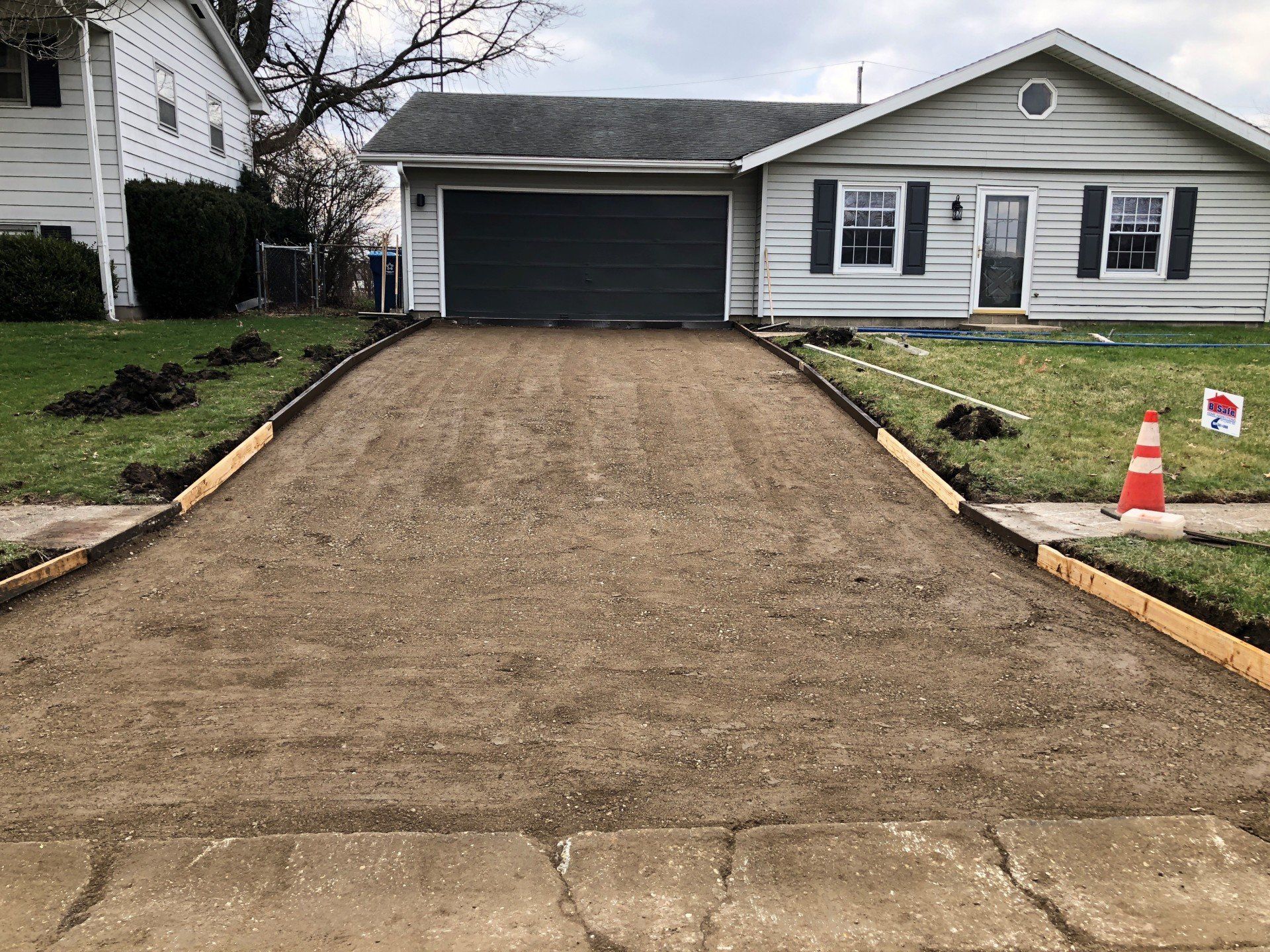 Driveway being prepared for paving, with wooden borders and a house in the background.
