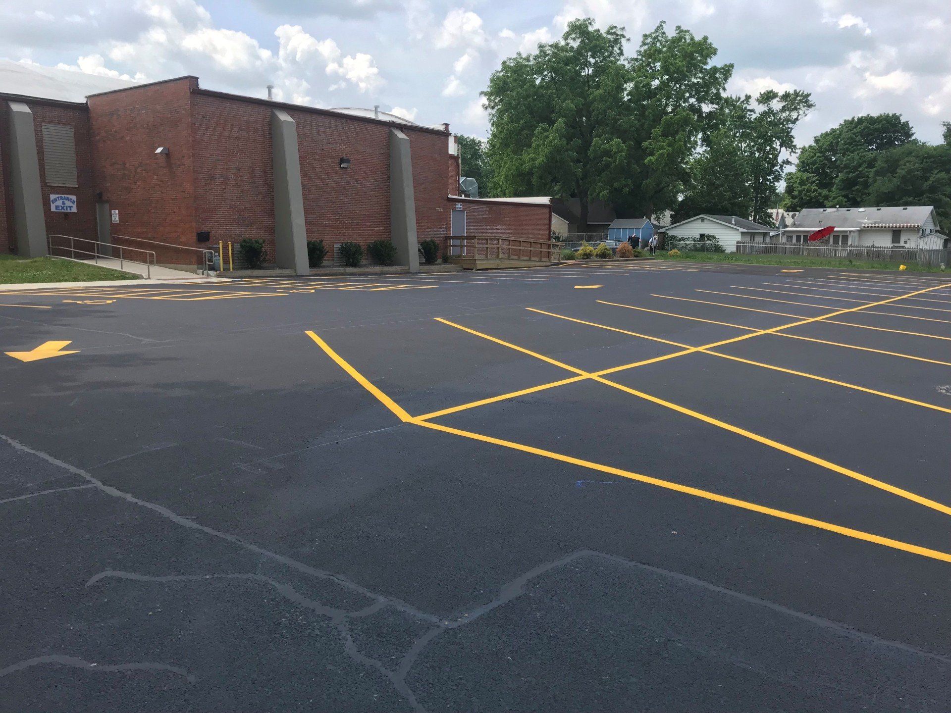 Exterior view of a newly paved parking lot with yellow painted lines. A brick building is in the background.