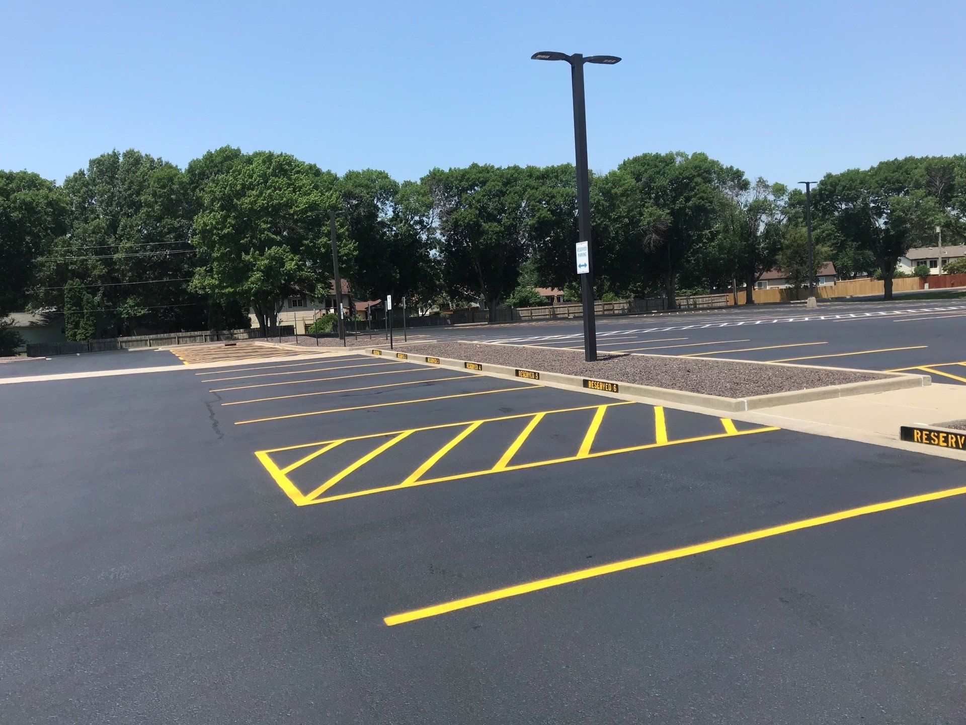 Newly paved parking lot with yellow painted lines and a light post.