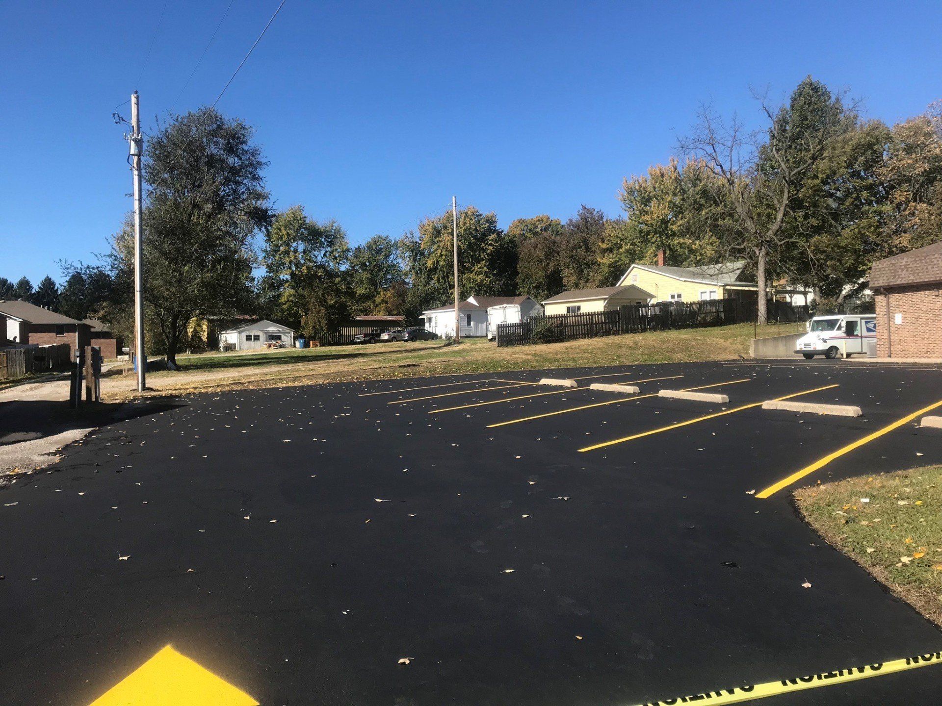 Asphalt parking lot with yellow markings, houses in the background, clear blue sky.