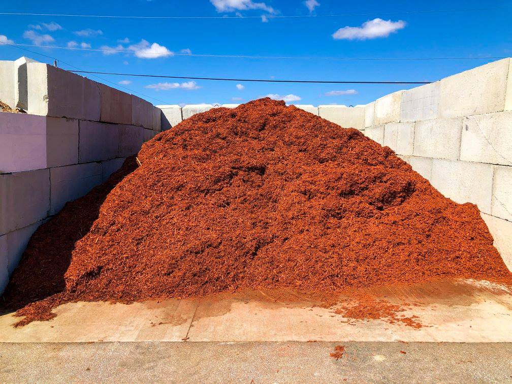 Pile of red mulch inside concrete retaining walls under blue sky.