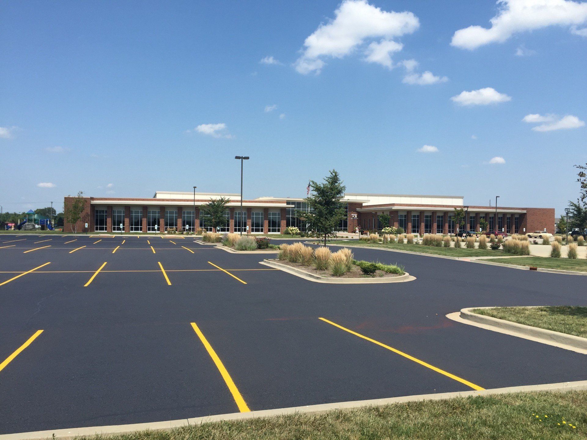 Large brick building with a black asphalt parking lot on a sunny day.