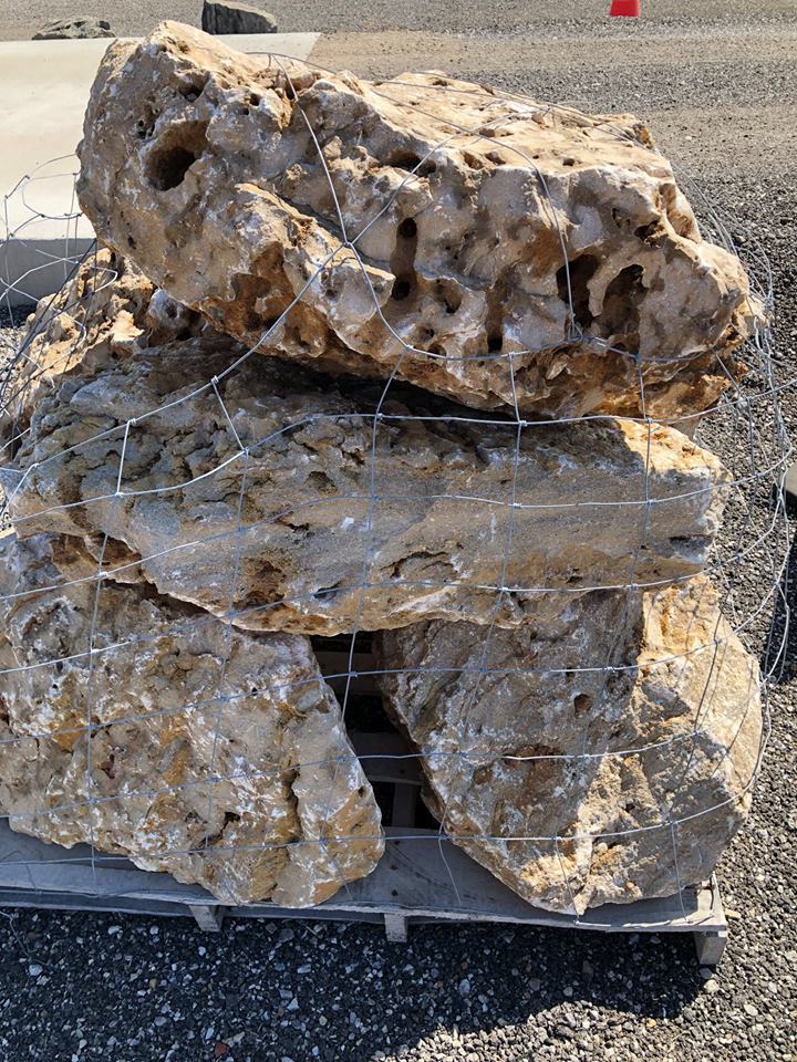 Pile of light brown, porous rocks on a wooden pallet, bound with wire.