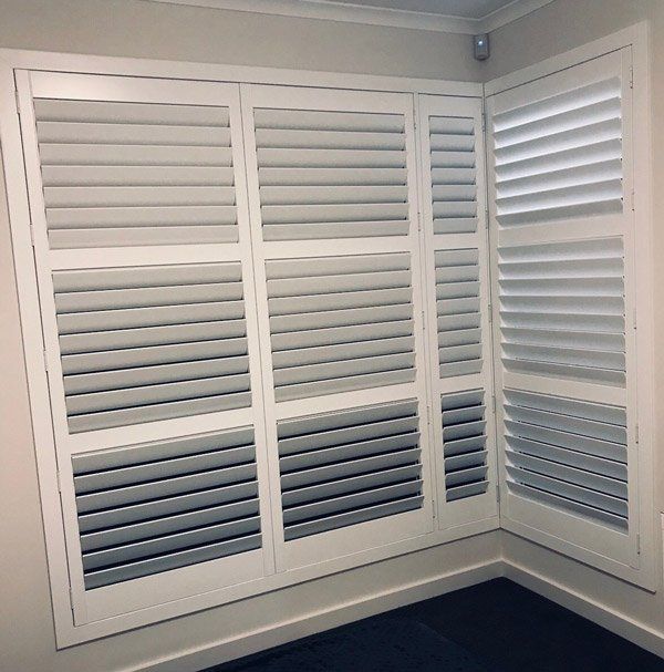 White, louvered shutters on a corner window. The shutters are closed, blocking the view.