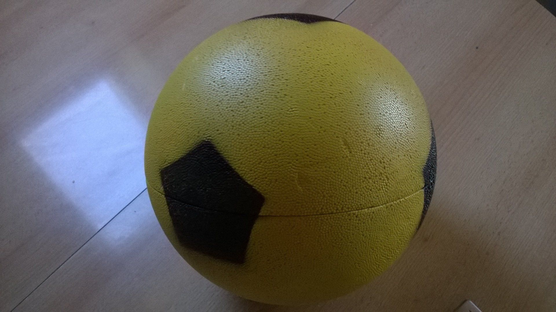 Auf einem Holztisch liegt ein gelb-schwarzer Fußball.
