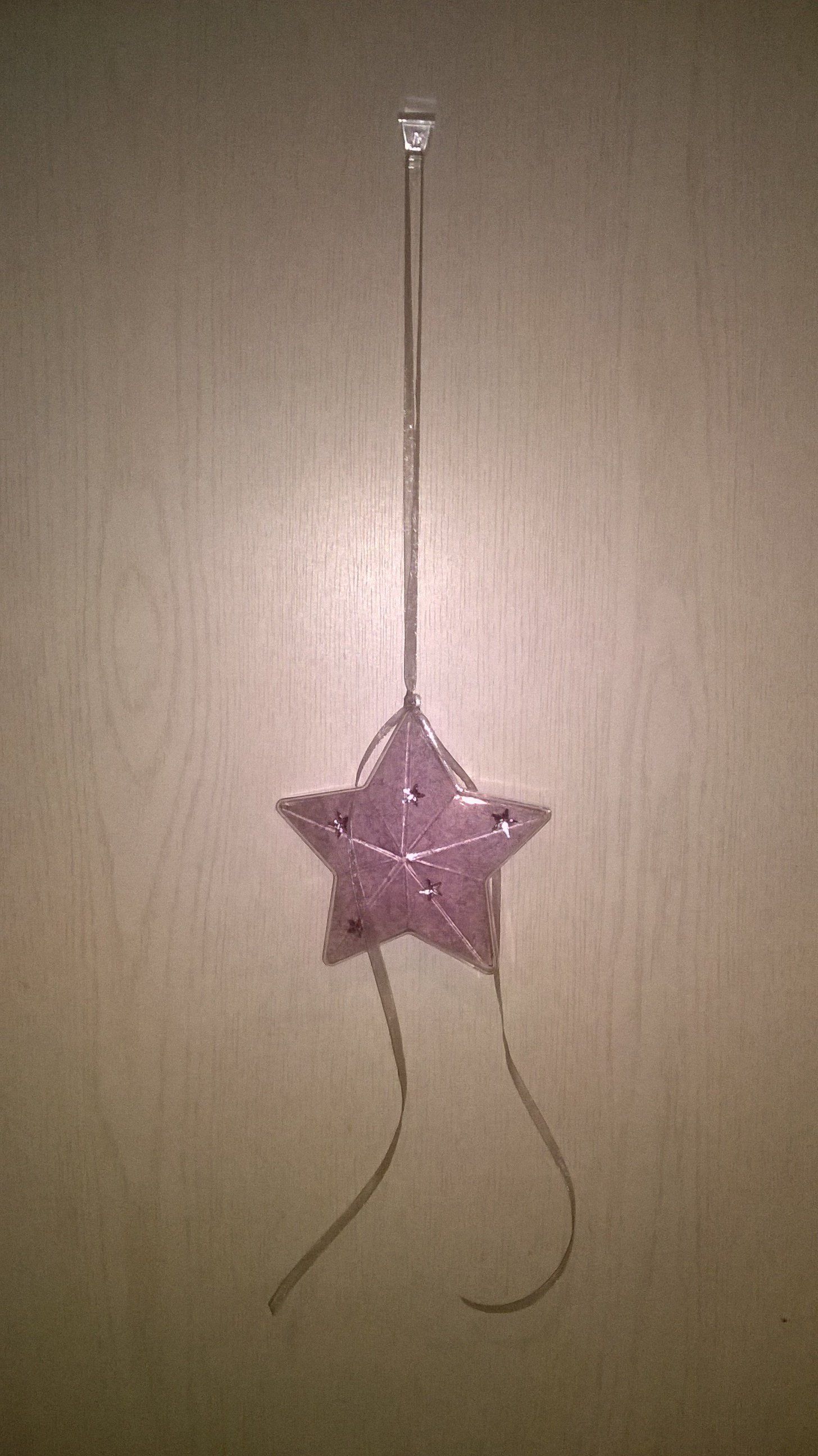 Ein rosa Stern, der an einer Schnur auf einer Holzoberfläche hängt.