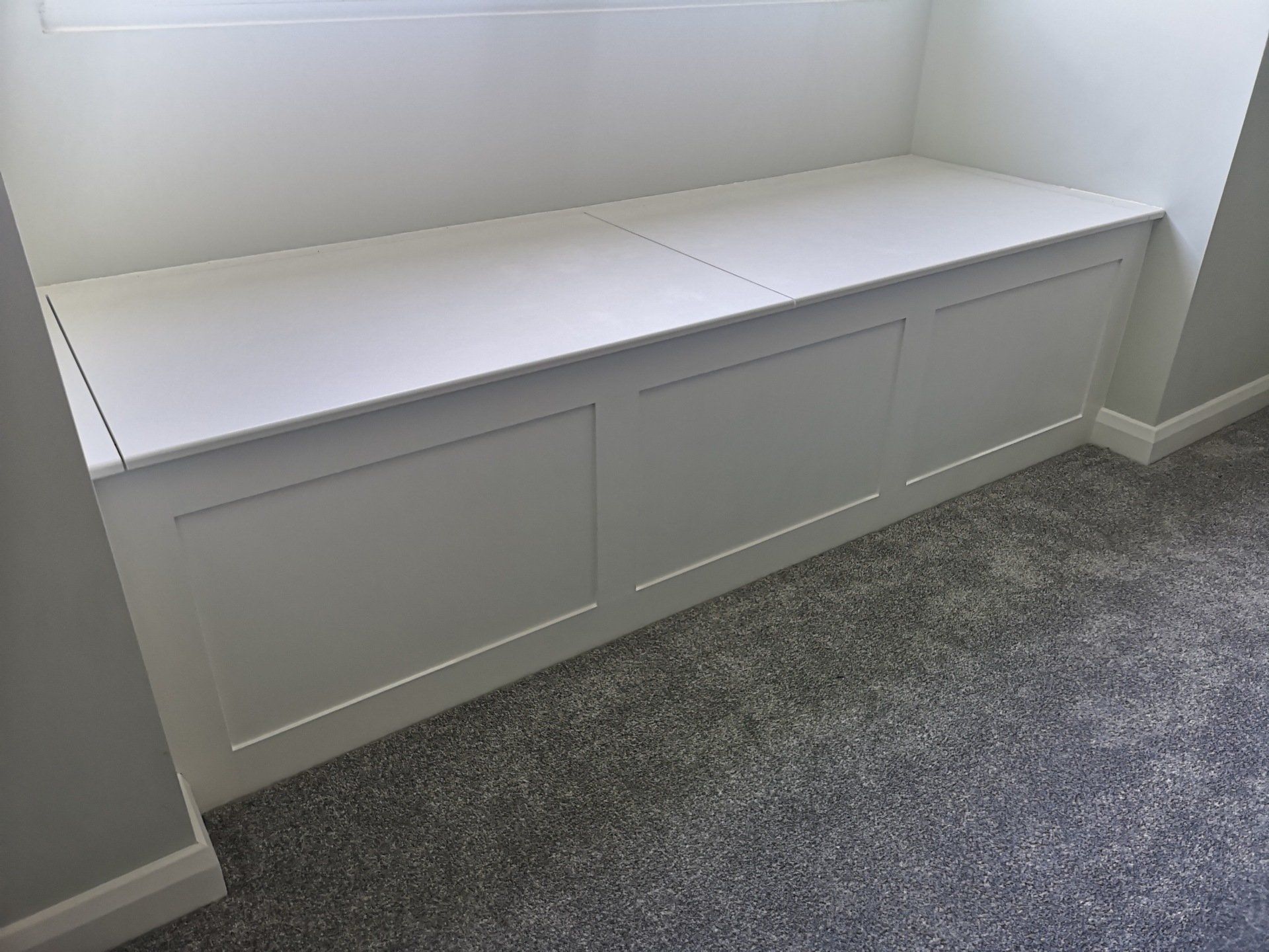 A bespoke made white window seat, made from MDF with shaker paneling and lift up lid for storage underneath.