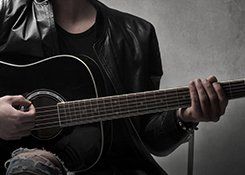 A leather-jacketed man strumming a black guitar