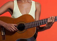 A lady in a cream vest top, playing an acoustic guitar