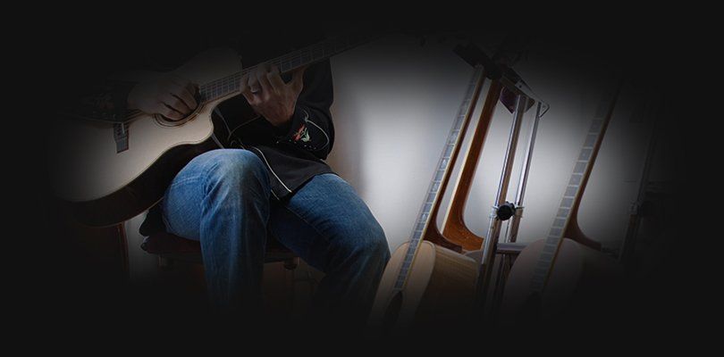 Two guitars and a microphone beside a seated guitarist in jenas