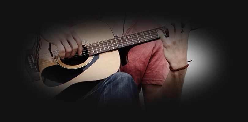 A man sitting with an acoustic guitar on his knee