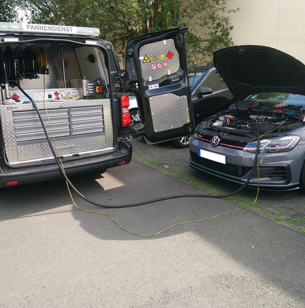 Ein Auto bekommt von einem Lieferwagen mit geöffneter Motorhaube den Tank abgepumpt.
