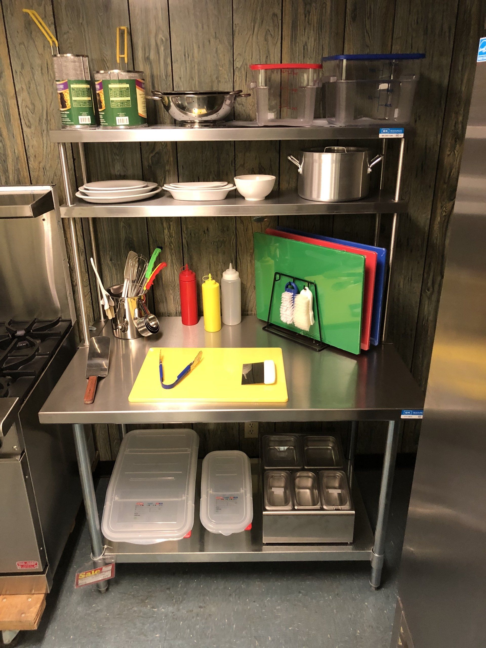 A stainless steel kitchen counter with a cutting board and condiments on it.