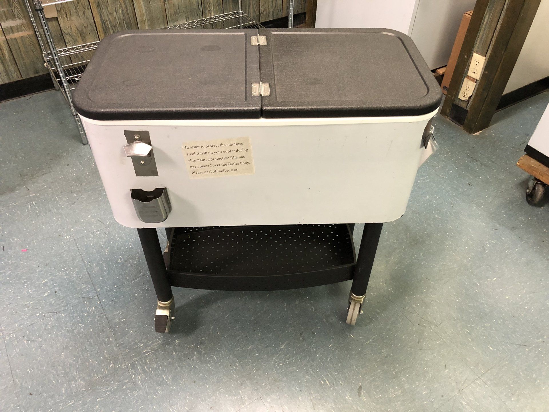 A white cooler on wheels is sitting on a blue floor.