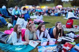 A group of young girls are laying on blankets in the grass watching a movie.