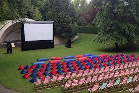 A large inflatable screen is sitting on top of a lush green field surrounded by chairs.