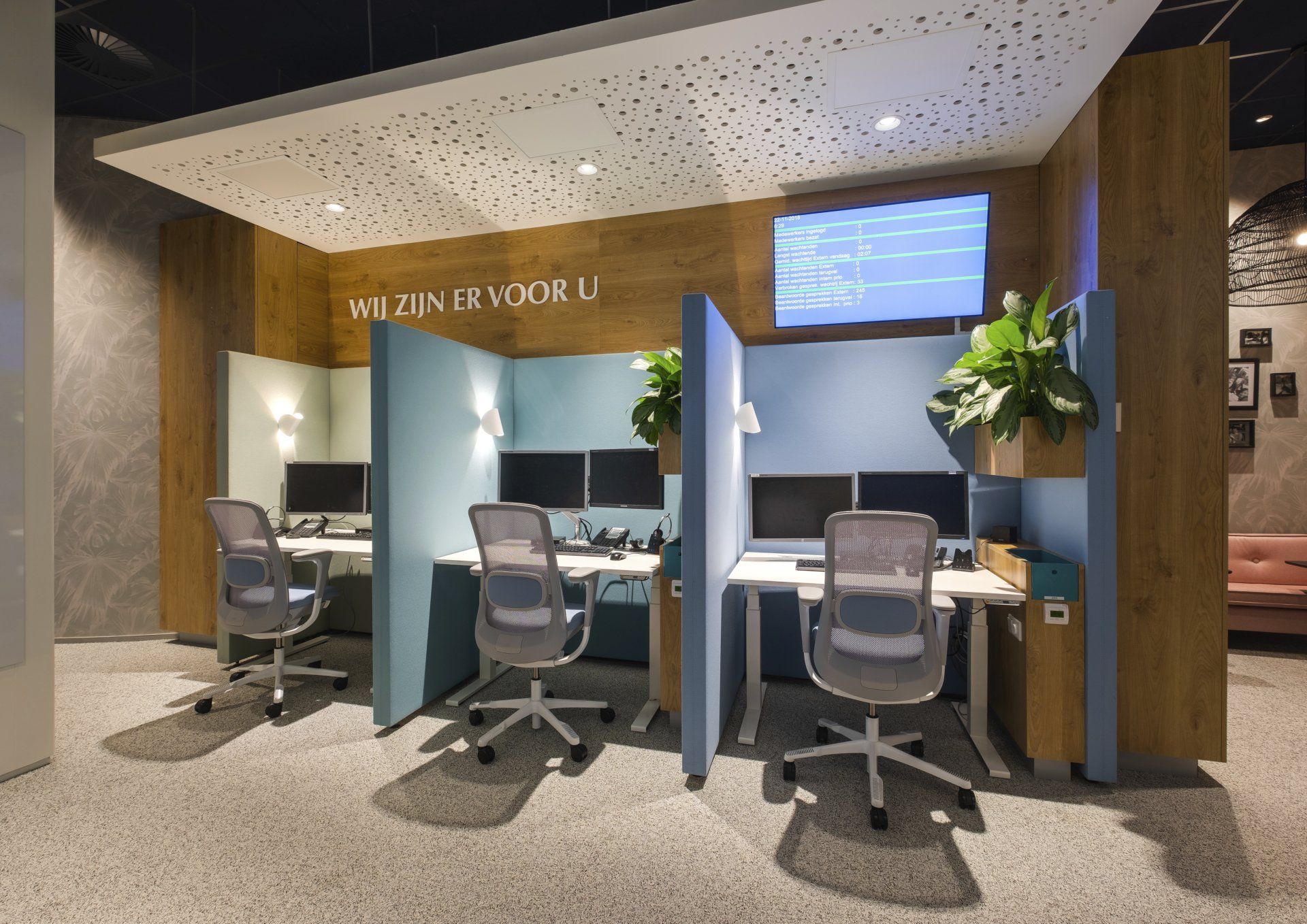 Drie afzonderlijke werkplekken, gescheiden door blauwe privacywanden, met lichtgekleurde bureaus, stoelen en beeldschermen in het callcenter van Gemeentehuis van Rijswijk, interieurontwerp door KuóStudio