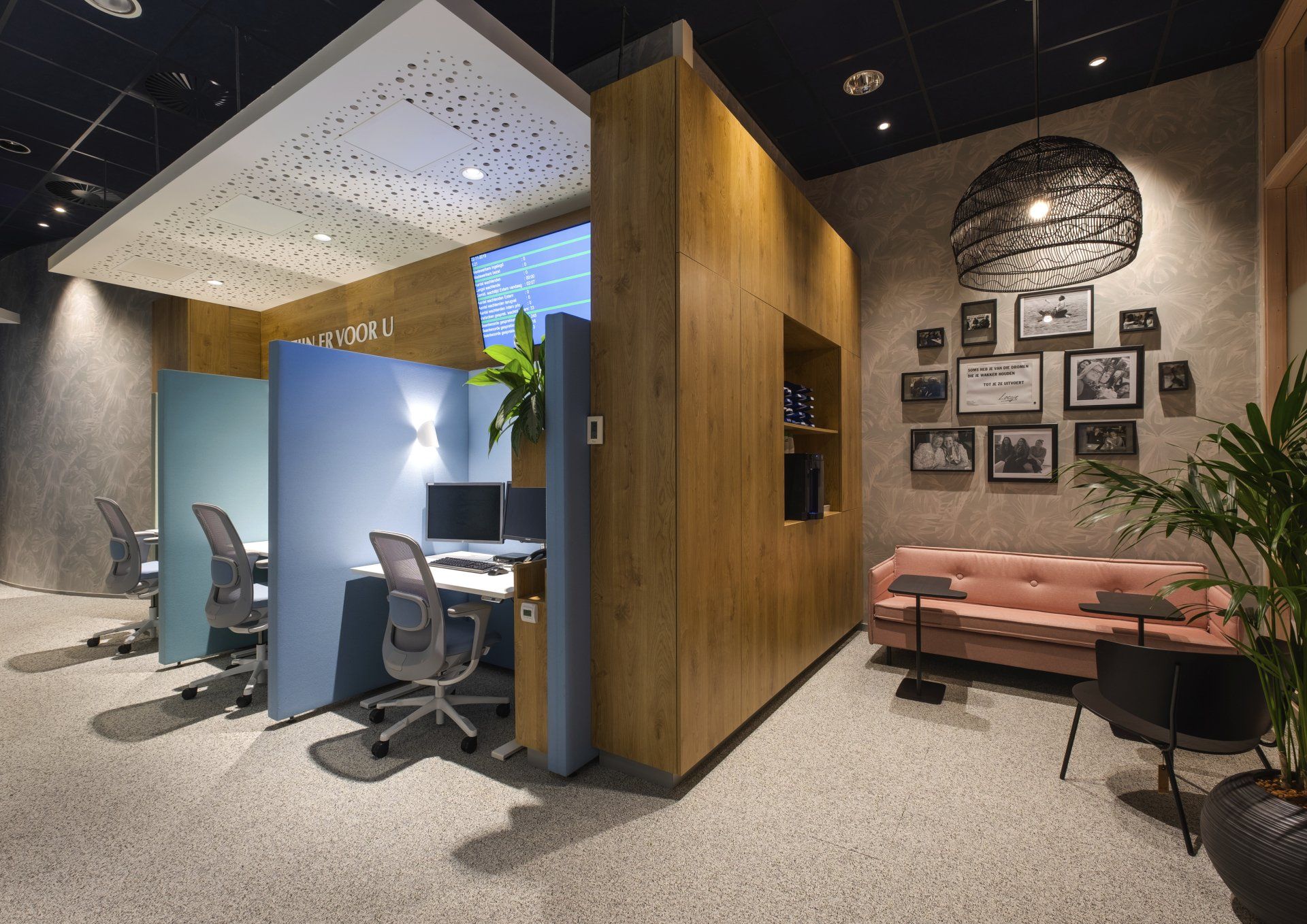 Moderne kantoorruimte met individuele werkplekken met blauwe scheidingswanden, een roze bank en een fotowand met ingelijste kunstwerken in het klant contact centrum van het Gemeentehuis van Rijswijk, interieurontwerp door KuóStudio