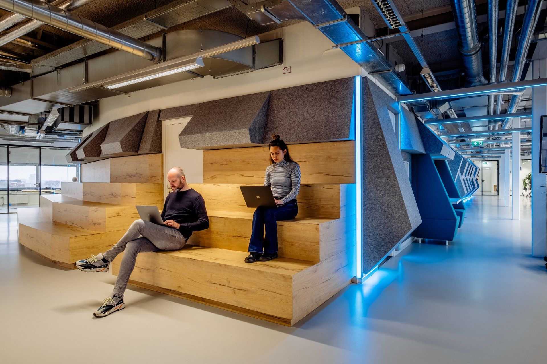 Twee mensen werken op laptops, zittend op tribune in het werkcafé in de moderne, industriële kantoorruimte van Shypple in Rotterdam, interieurontwerp voor KuóStudio