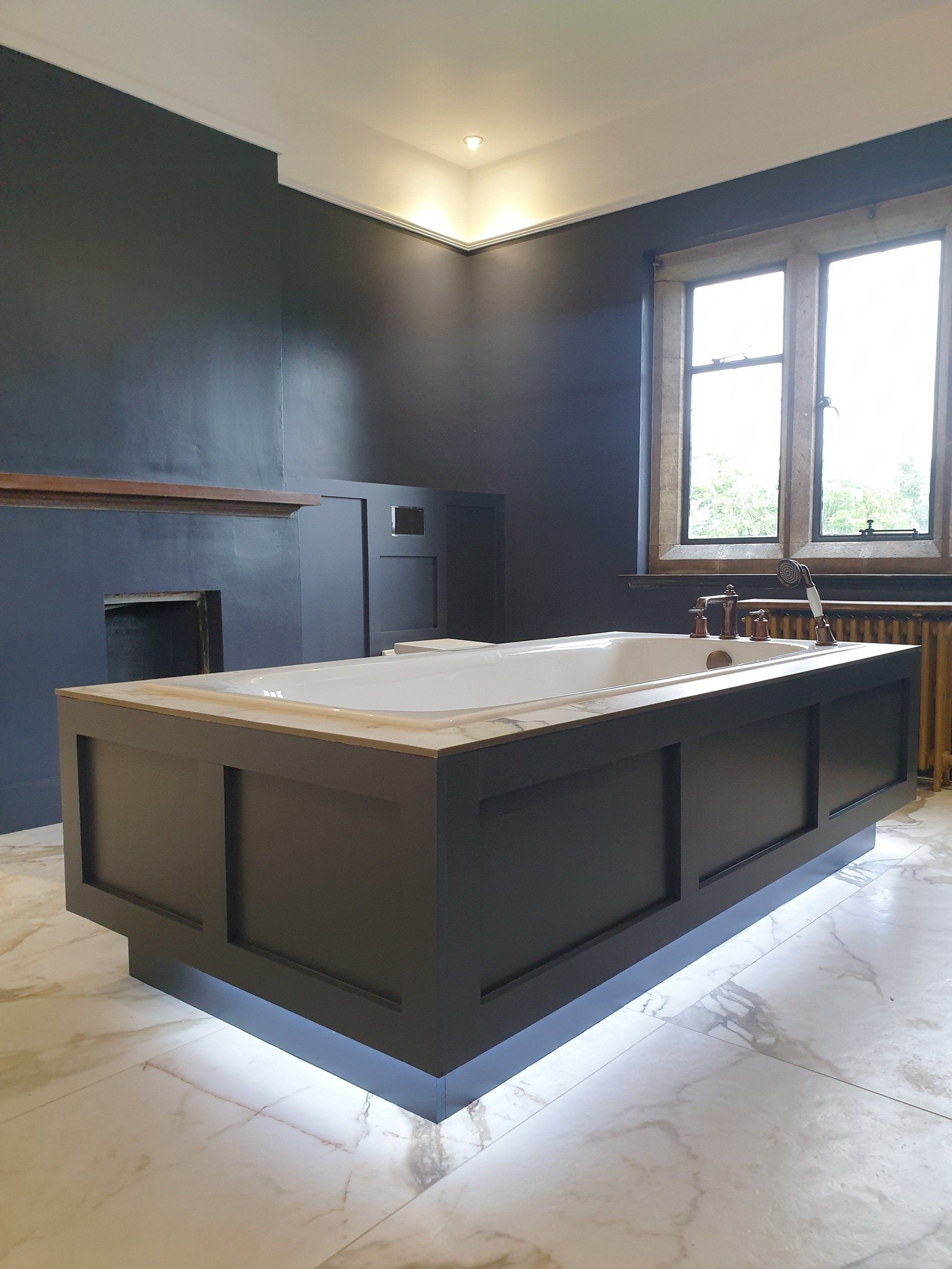Modern freestanding bath with dark panel and underlighting.