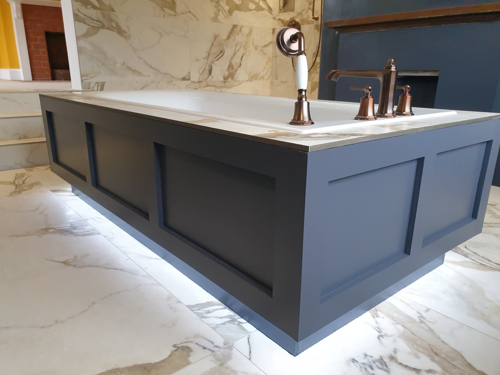 Dark bathroom vanity with marble worktop and gold tap.