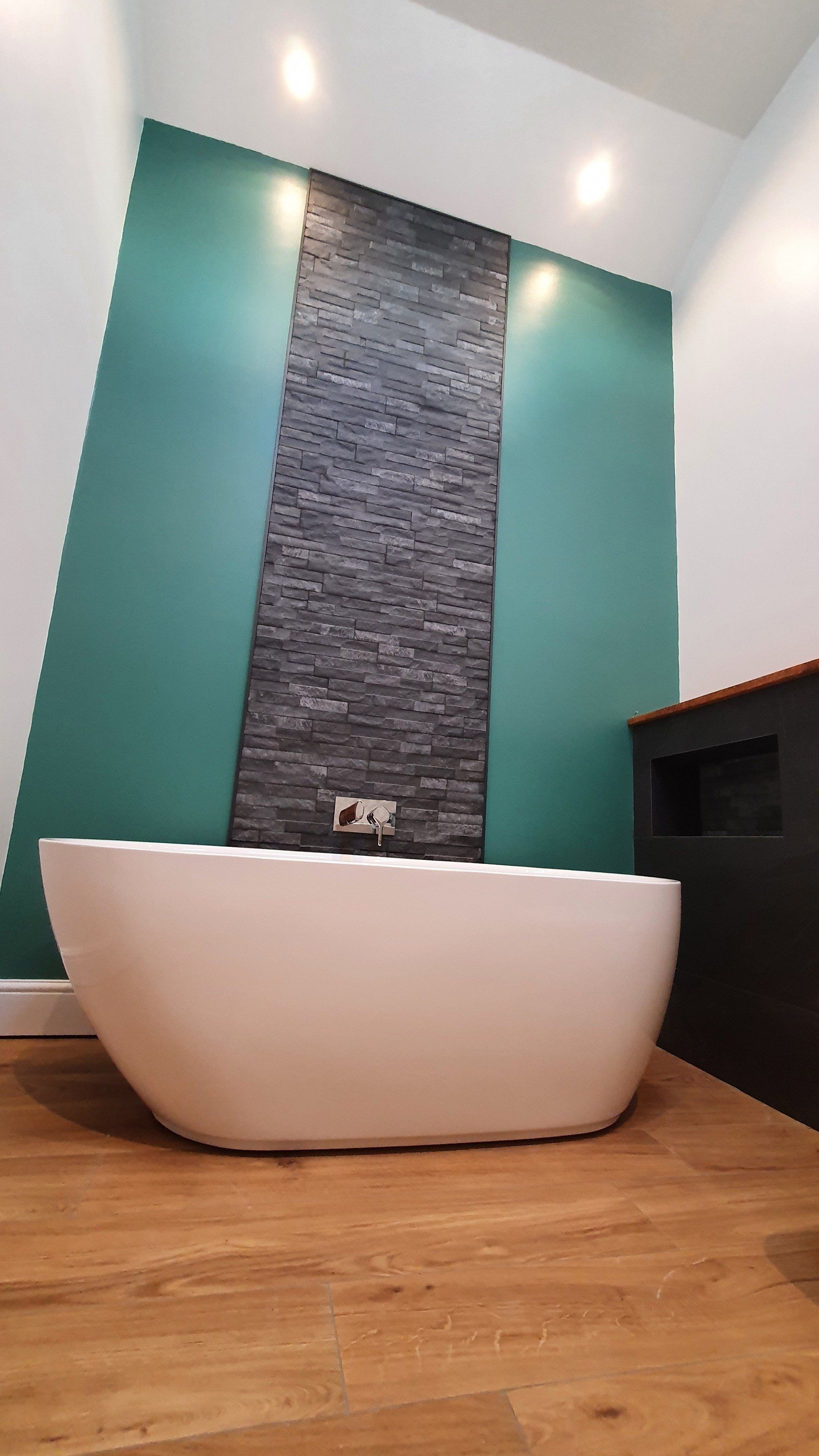 White freestanding bath against teal and stone-effect wall panels.