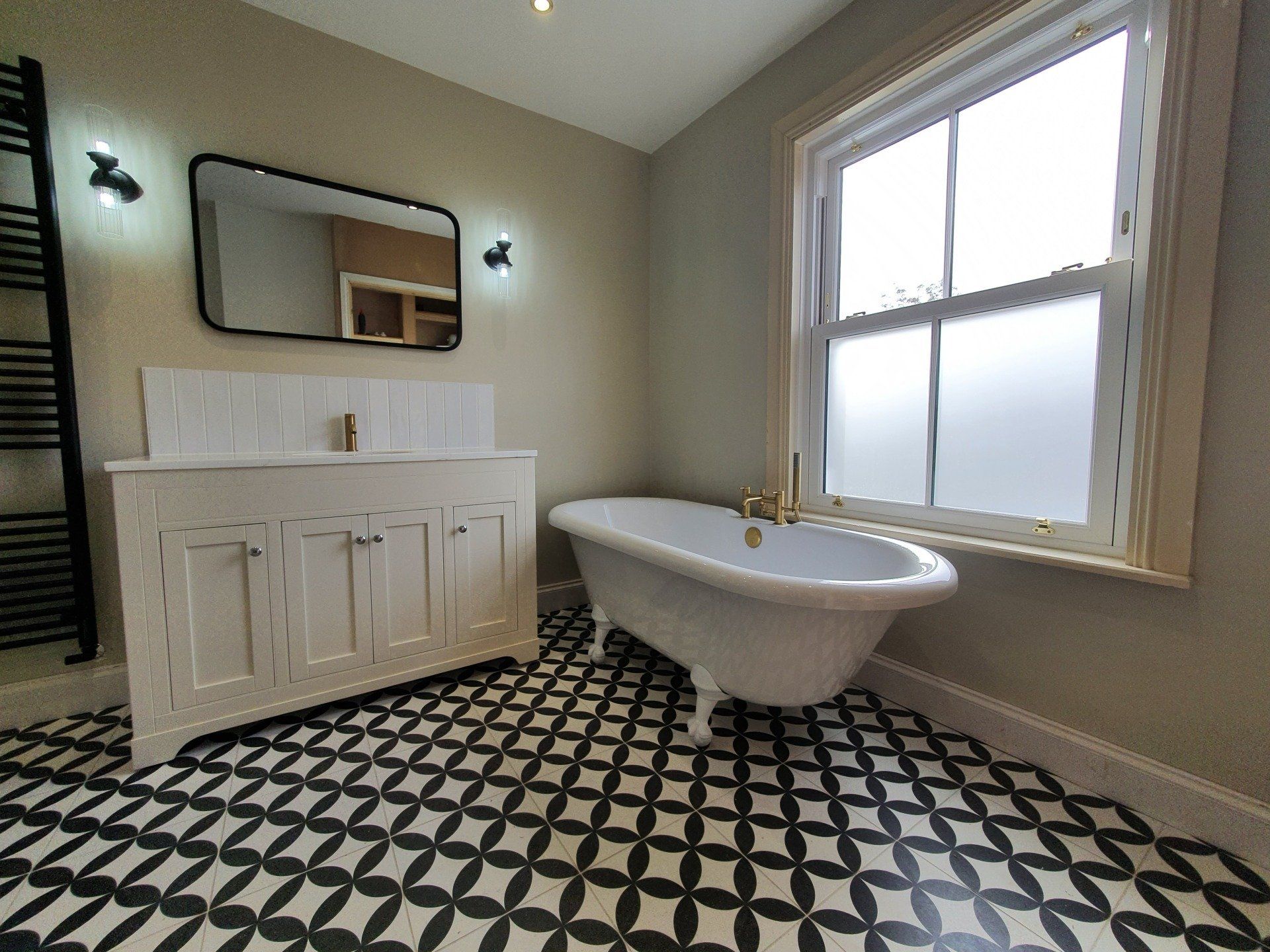 Bright bathroom with freestanding bath, double vanity and geometric flooring.