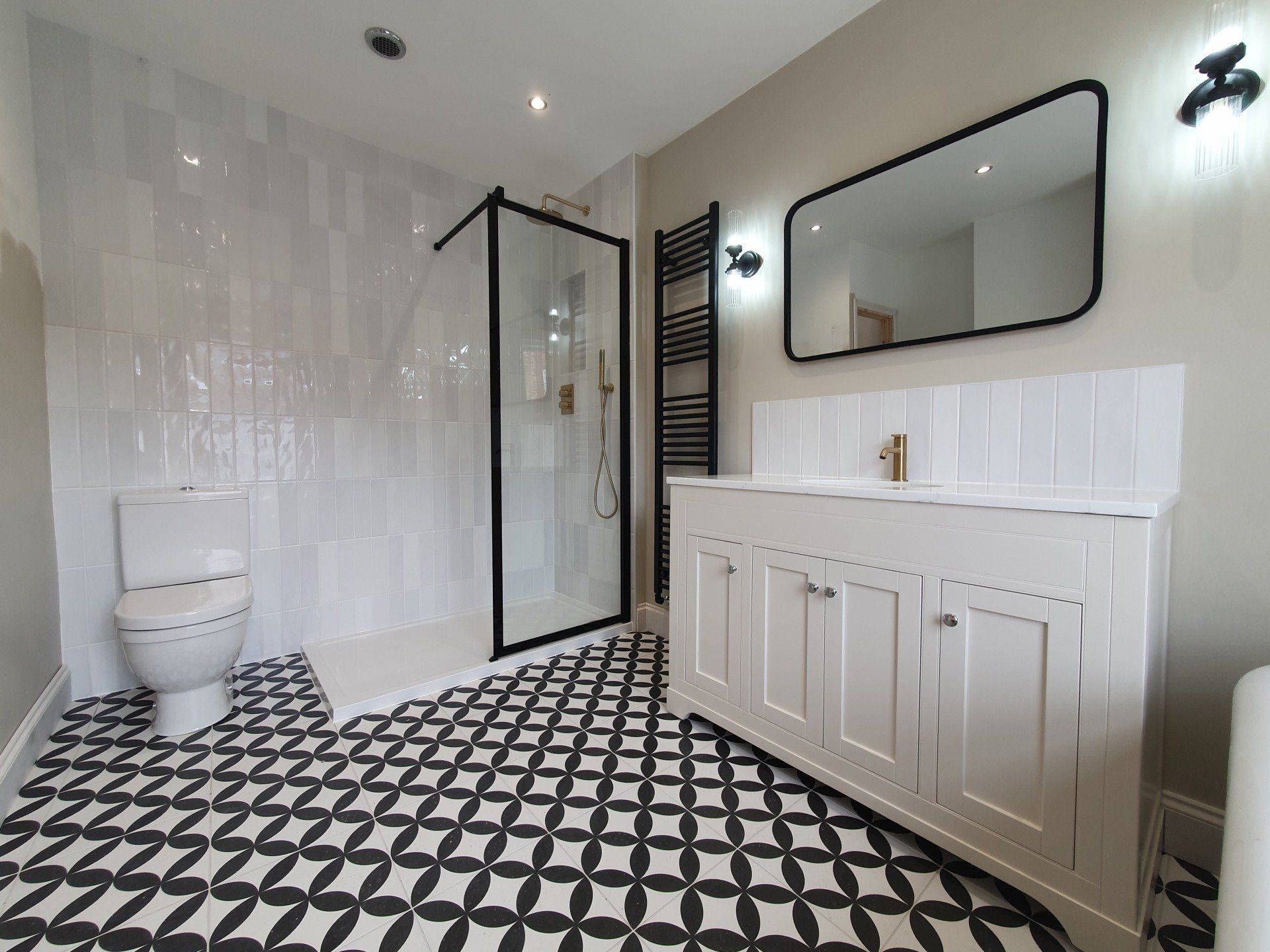 Modern bathroom with walk-in shower, white vanity and black patterned floor.