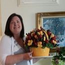 A woman is holding a tray of fruit and flowers.