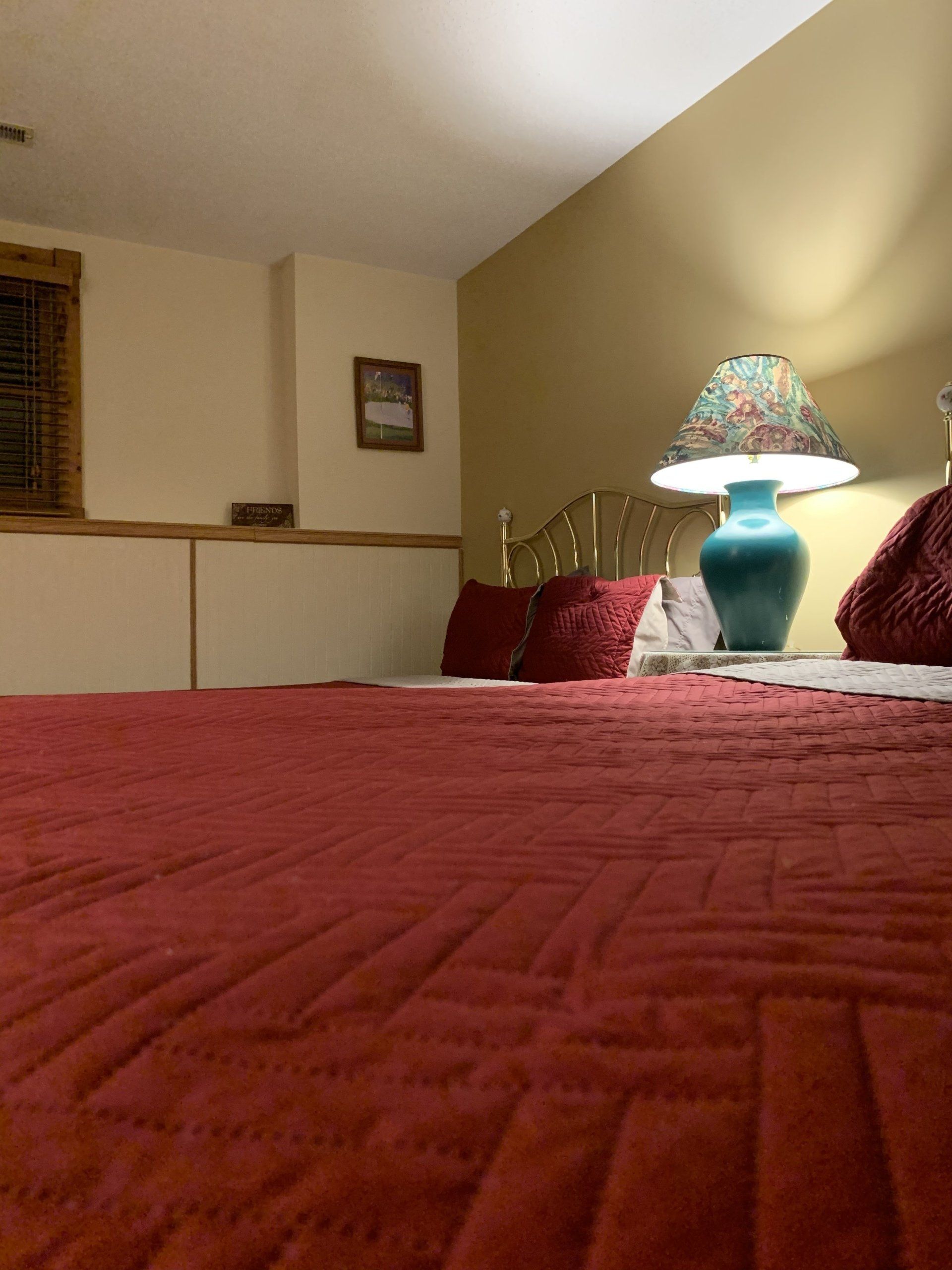 Red bed with a teal lamp on nightstand against beige walls.