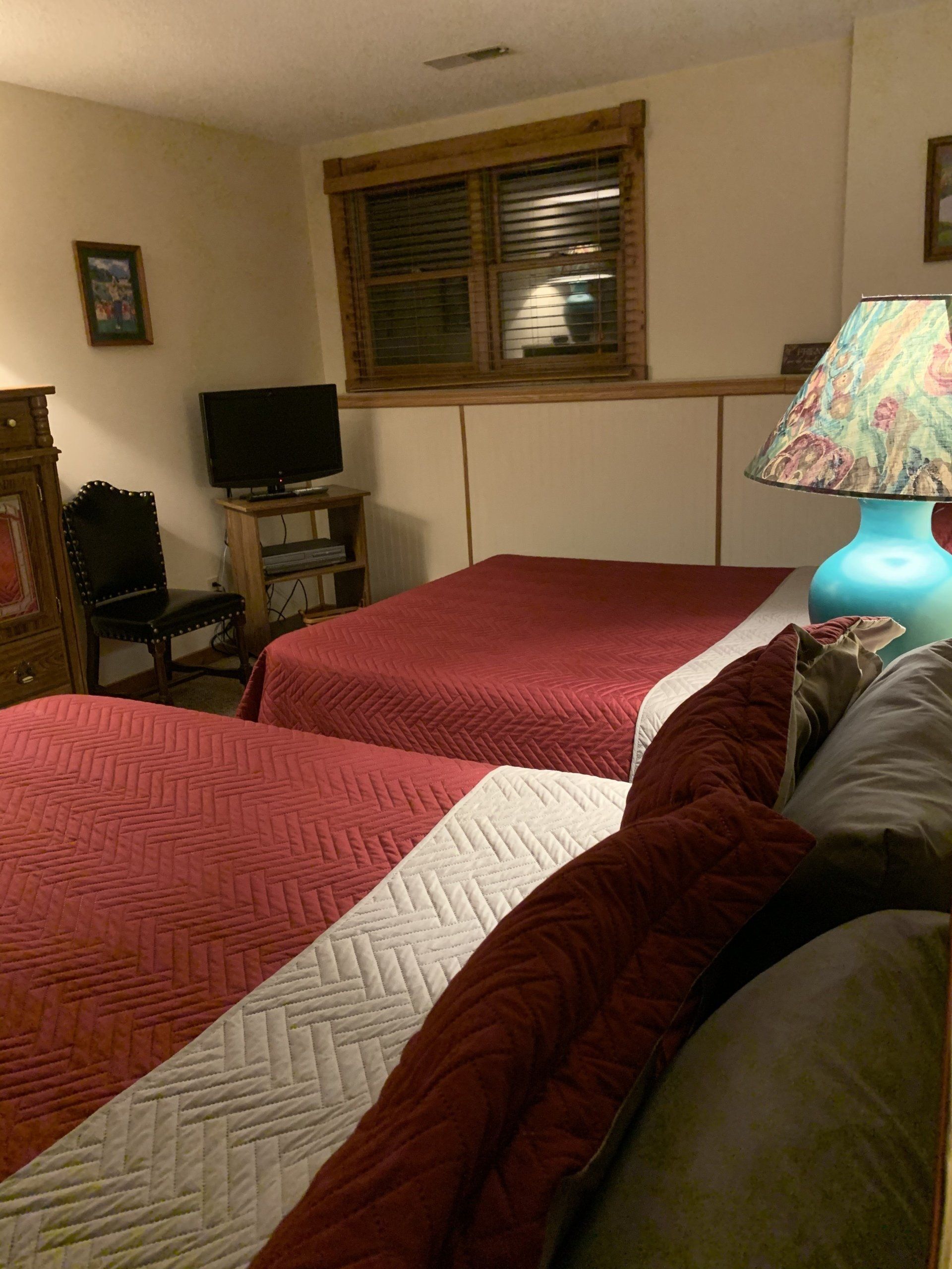 Two beds with red comforters in a room with a TV and a lamp.
