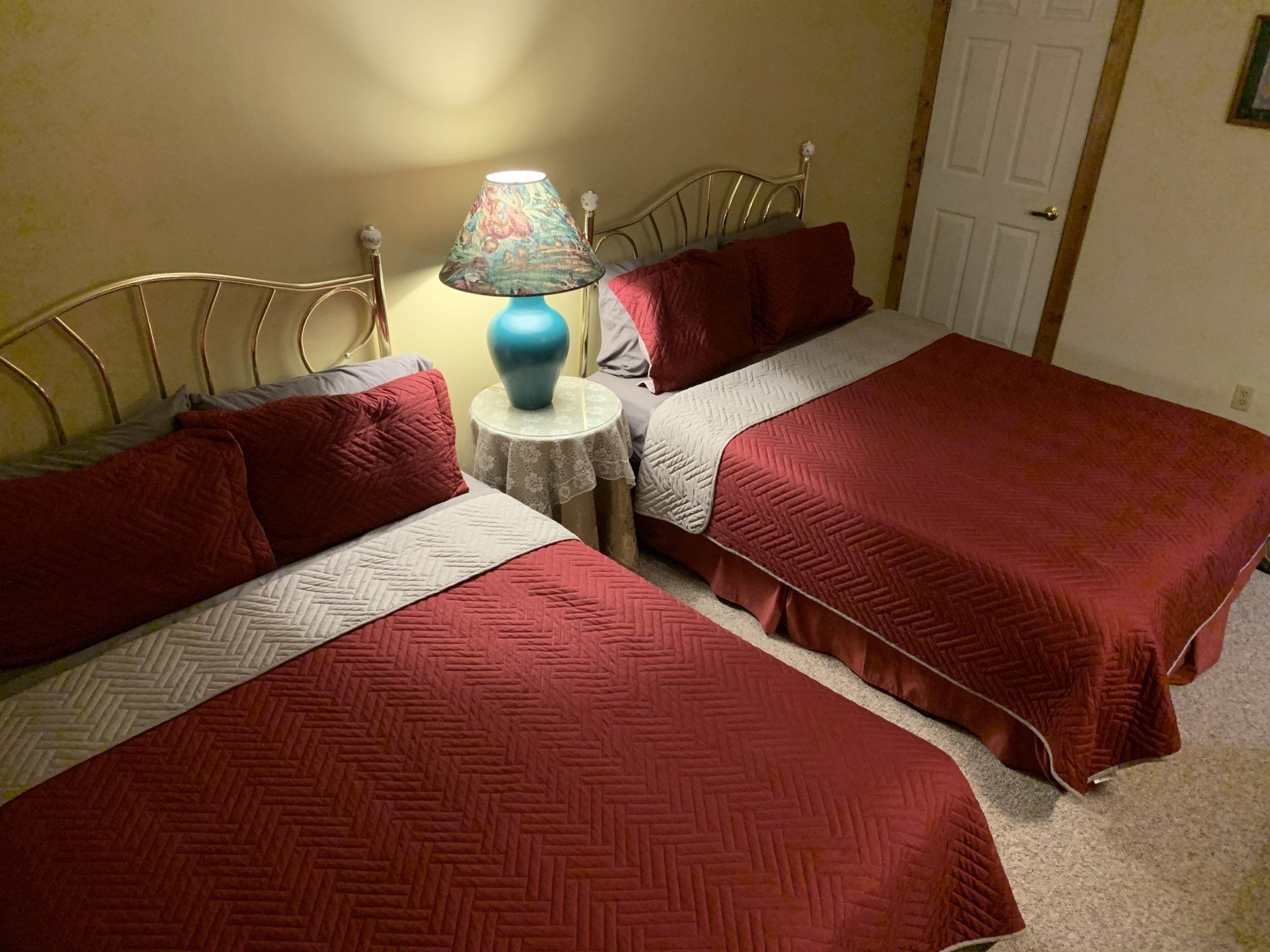 Two beds with red comforters and a lamp on a small table.