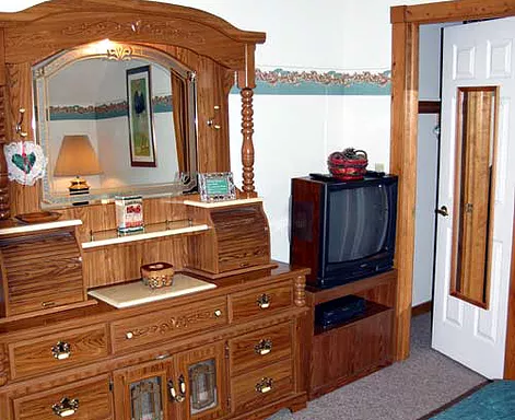 Wooden bedroom dresser with mirror, and a small television. Door to closet is on the right.