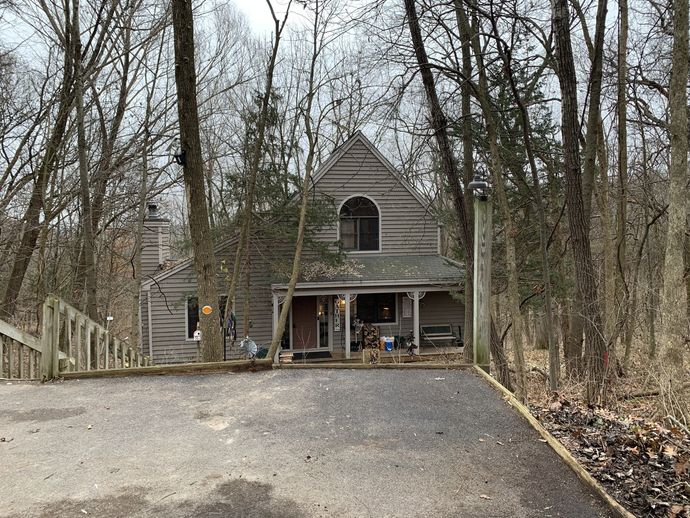 Log cabin nestled among trees, with a driveway and porch visible.