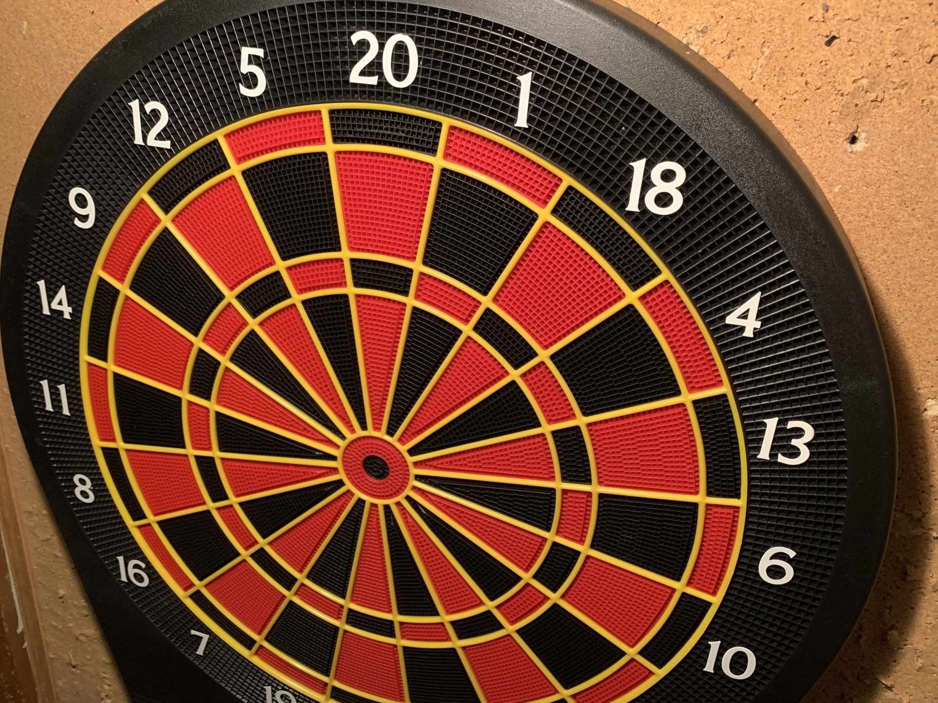 Dartboard with red, black, and yellow segments, mounted on a tan wall. Numbers are visible around the perimeter.