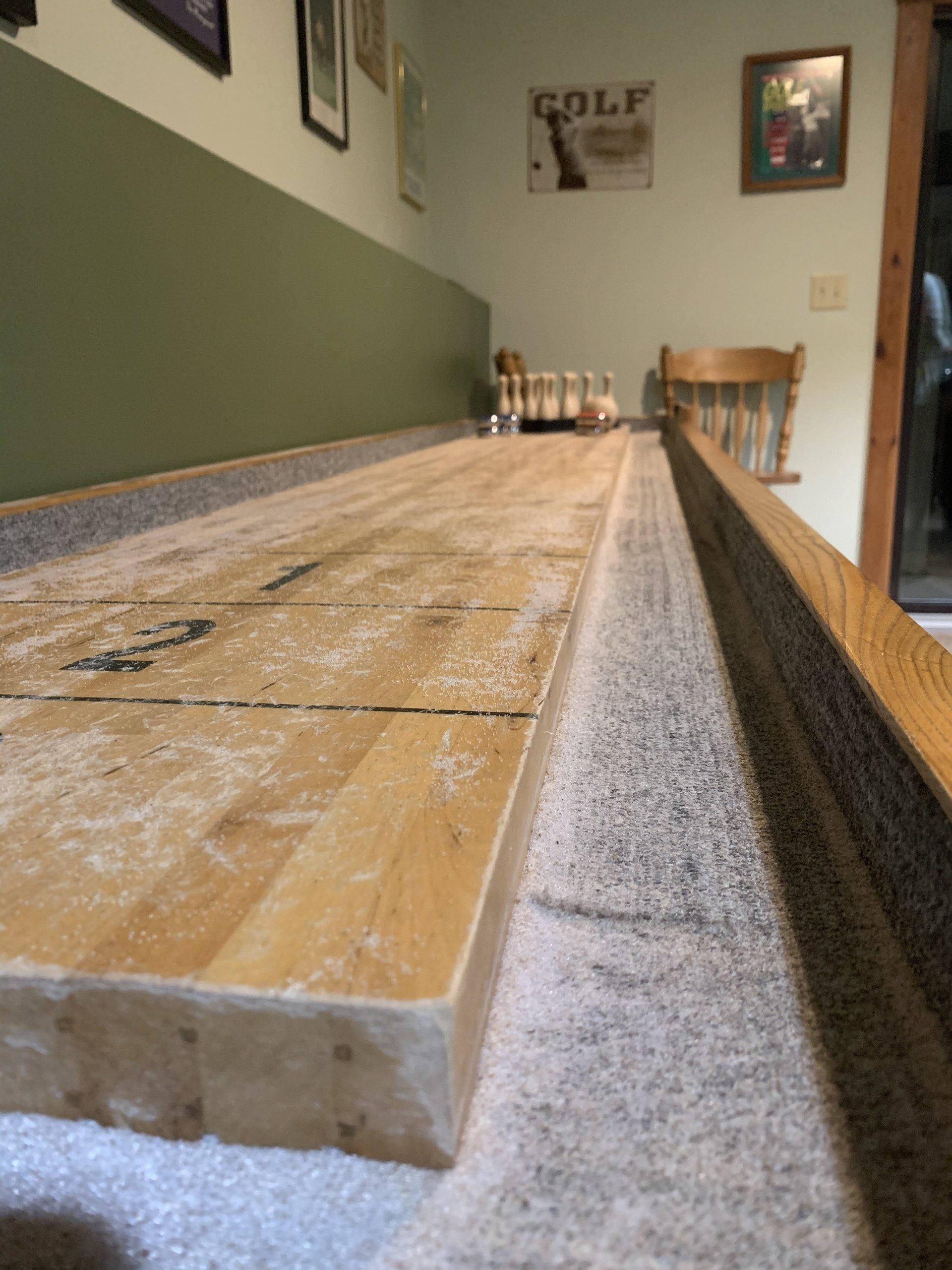 Shuffleboard table with a dusting of shuffleboard wax, pins, and a vintage golf sign.