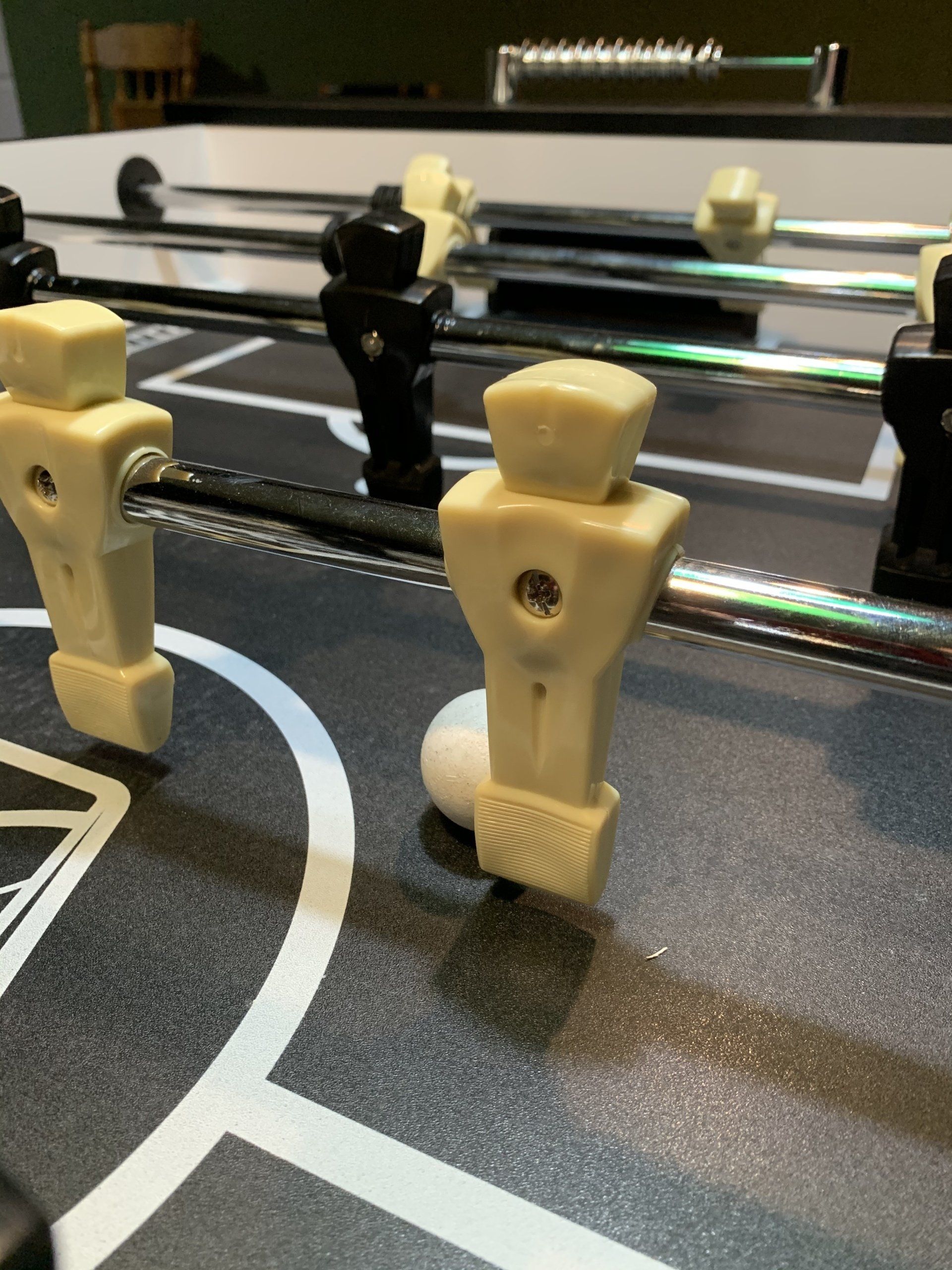 Foosball table with a white ball near a white player figure. Black and white game surface.
