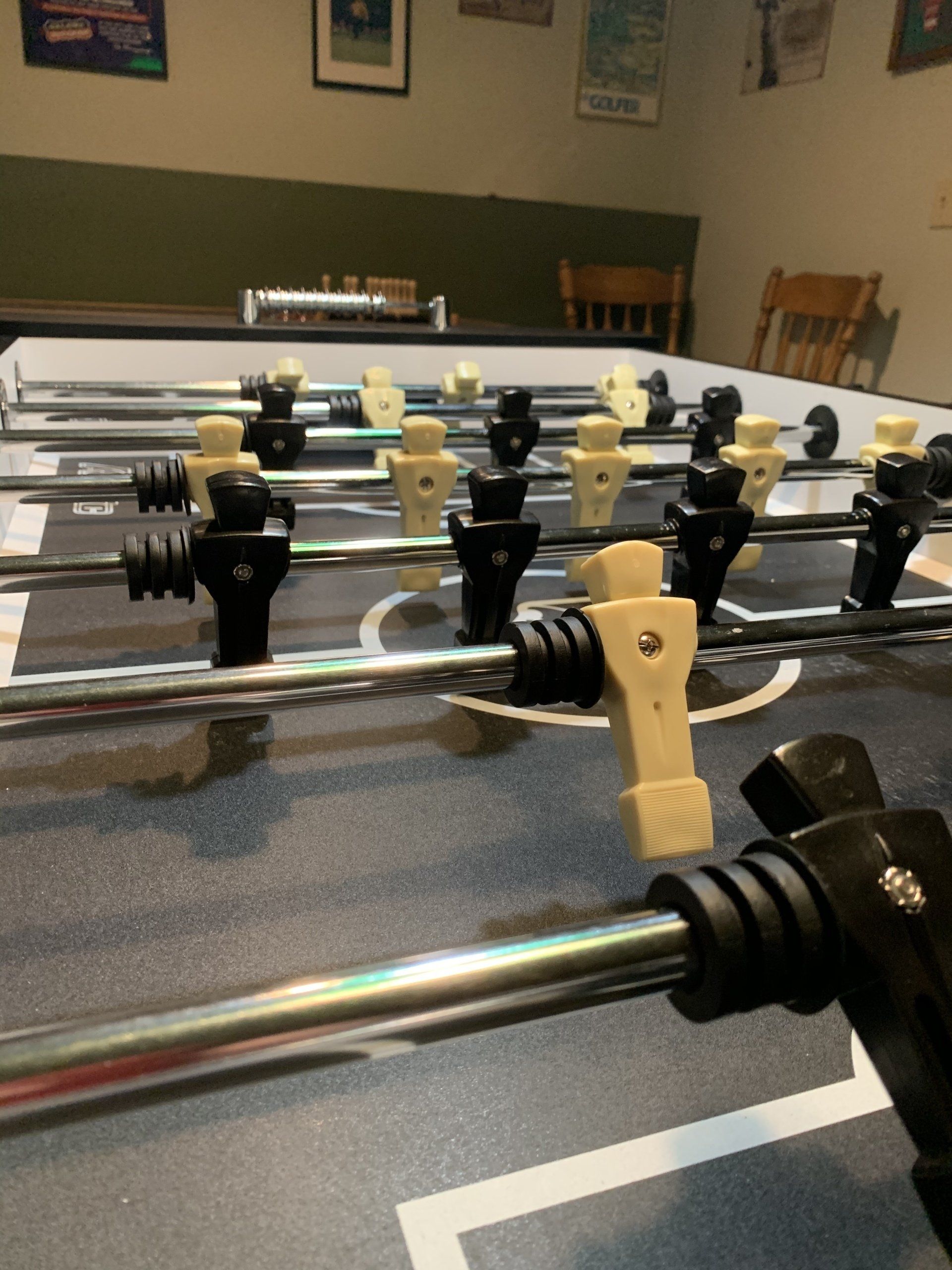Foosball table with black and tan players, ready for play, in a basement setting.