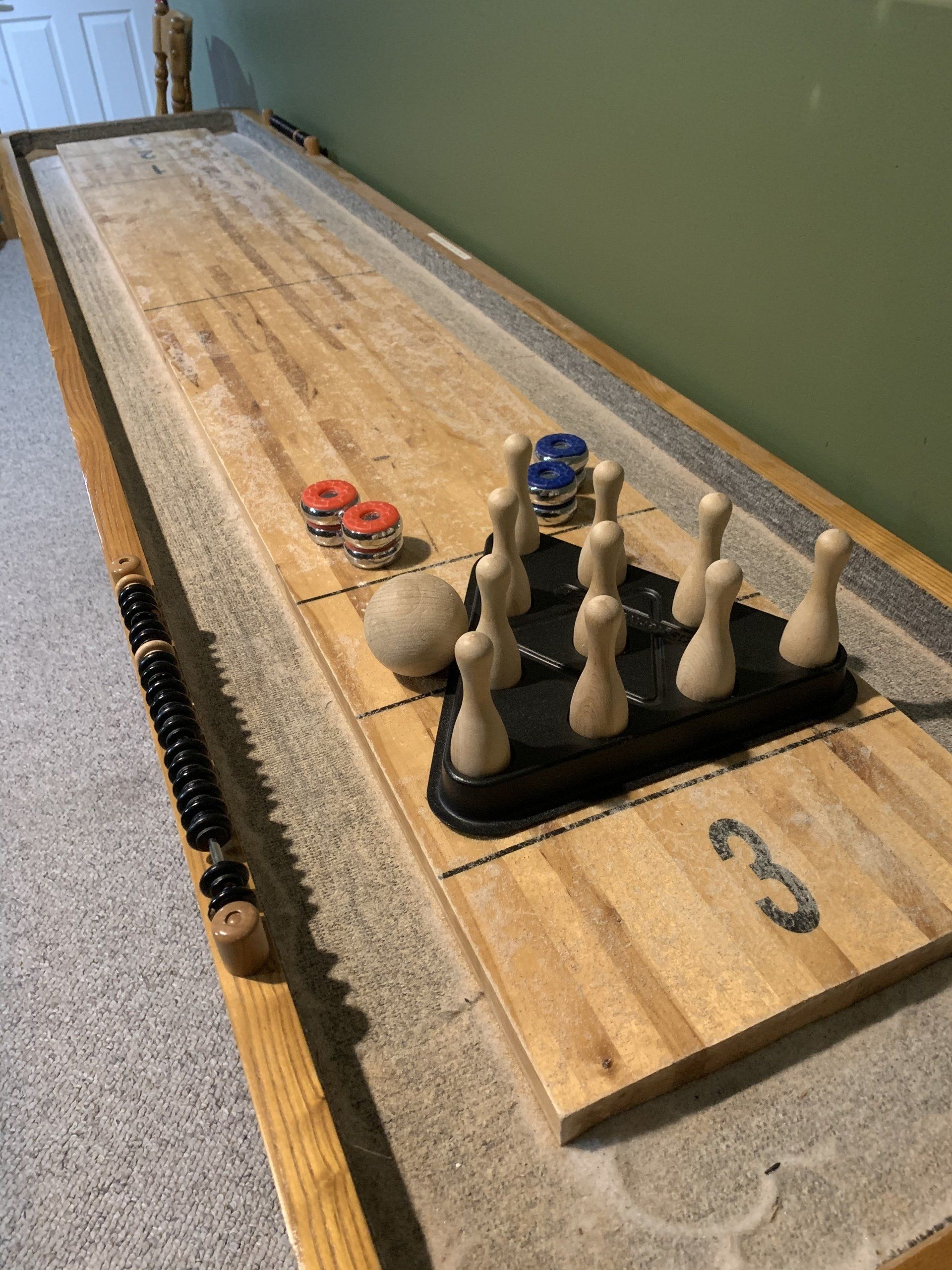 Shuffleboard game set up with pins, pucks, and a ball on a wooden playing surface.