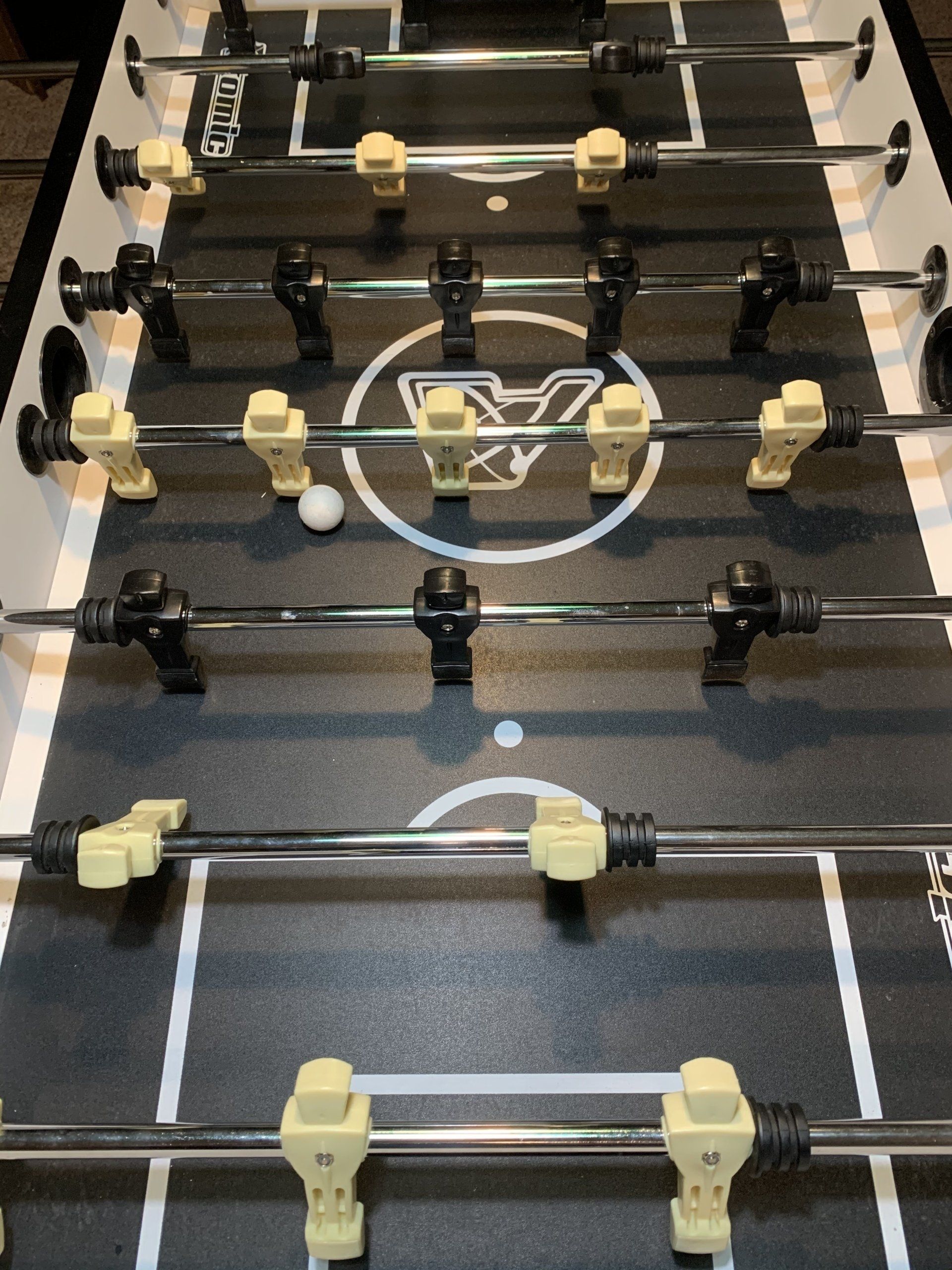 Foosball table with a white ball. Black and beige player figures are attached to the silver rods. The table has a white and black field.