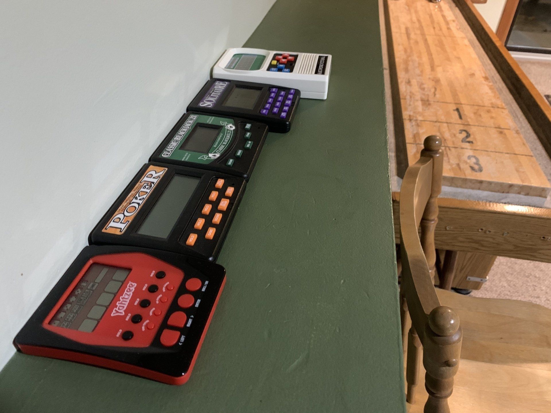 Row of handheld electronic games on a green shelf next to a shuffleboard table.