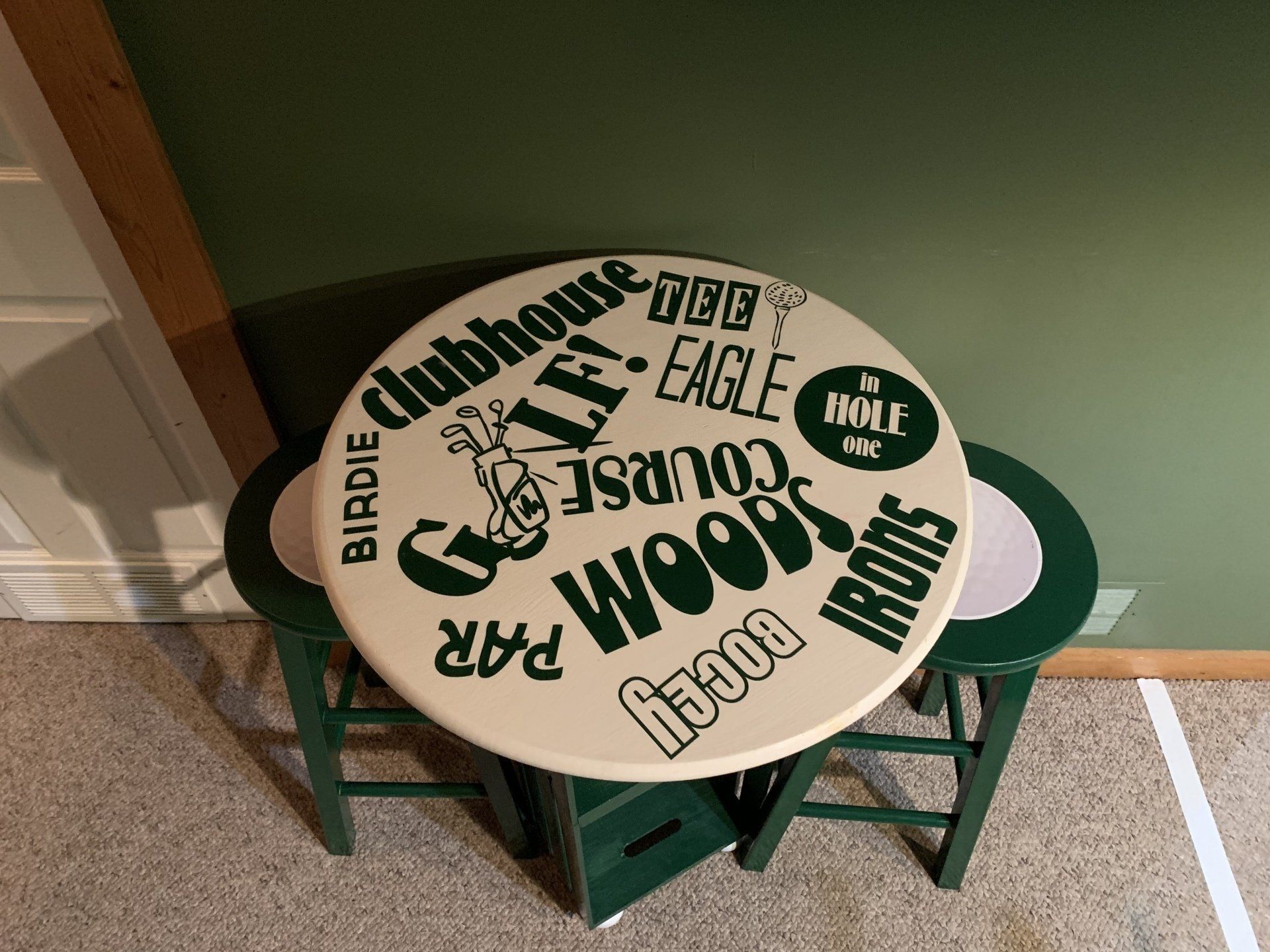 Round table with golf-themed words and designs on top, set on two green stools.