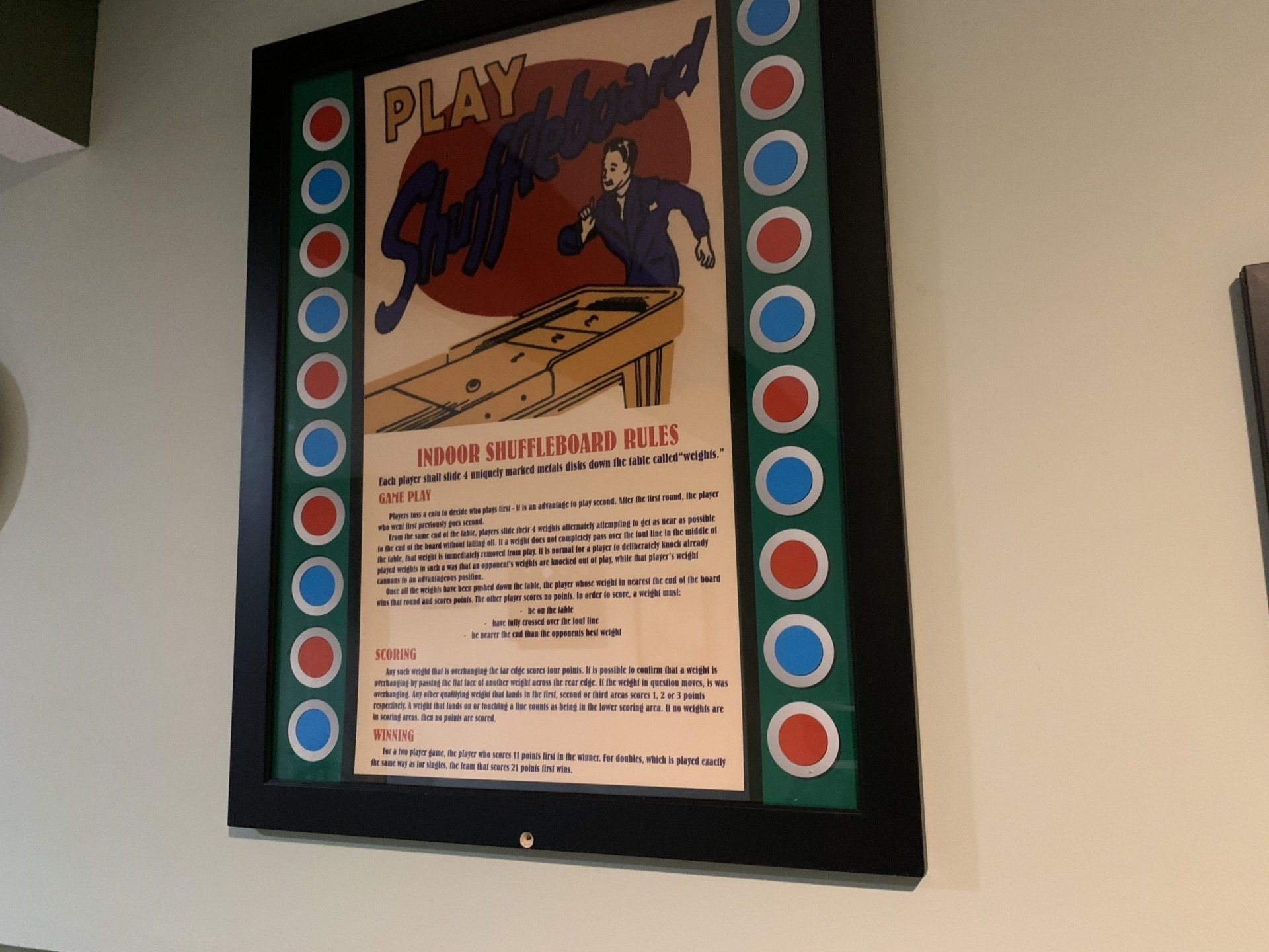 Framed vintage poster for shuffleboard game, with instructions and players in action. Red, blue, green colors.