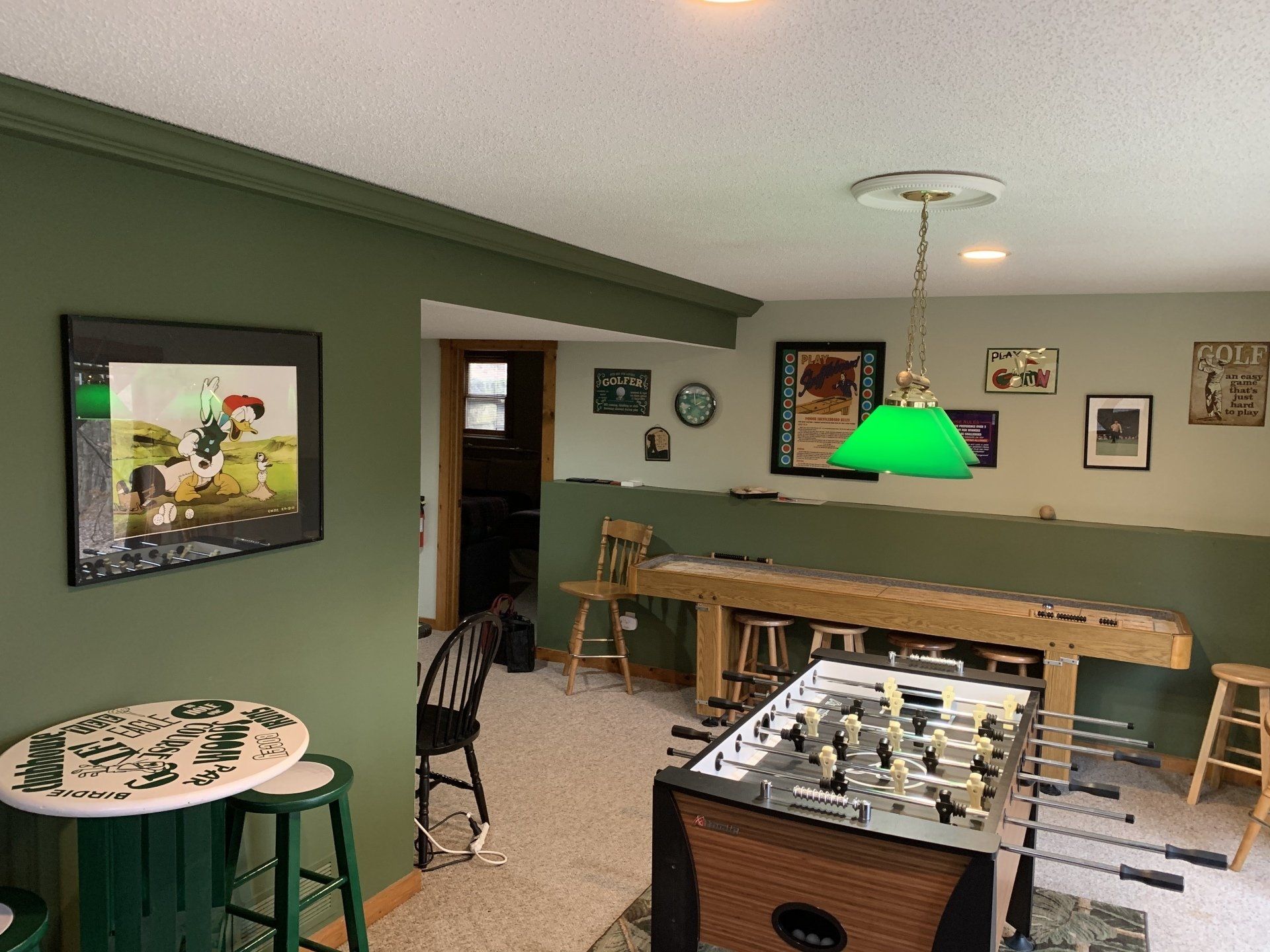 A game room with a foosball table, bar table, green walls, and a large wooden table.