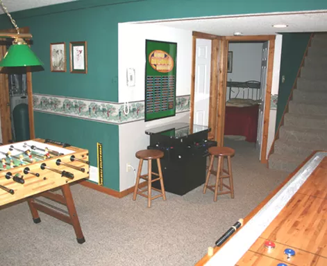 Game room with foosball, shuffleboard, and a bar area, painted green and beige.
